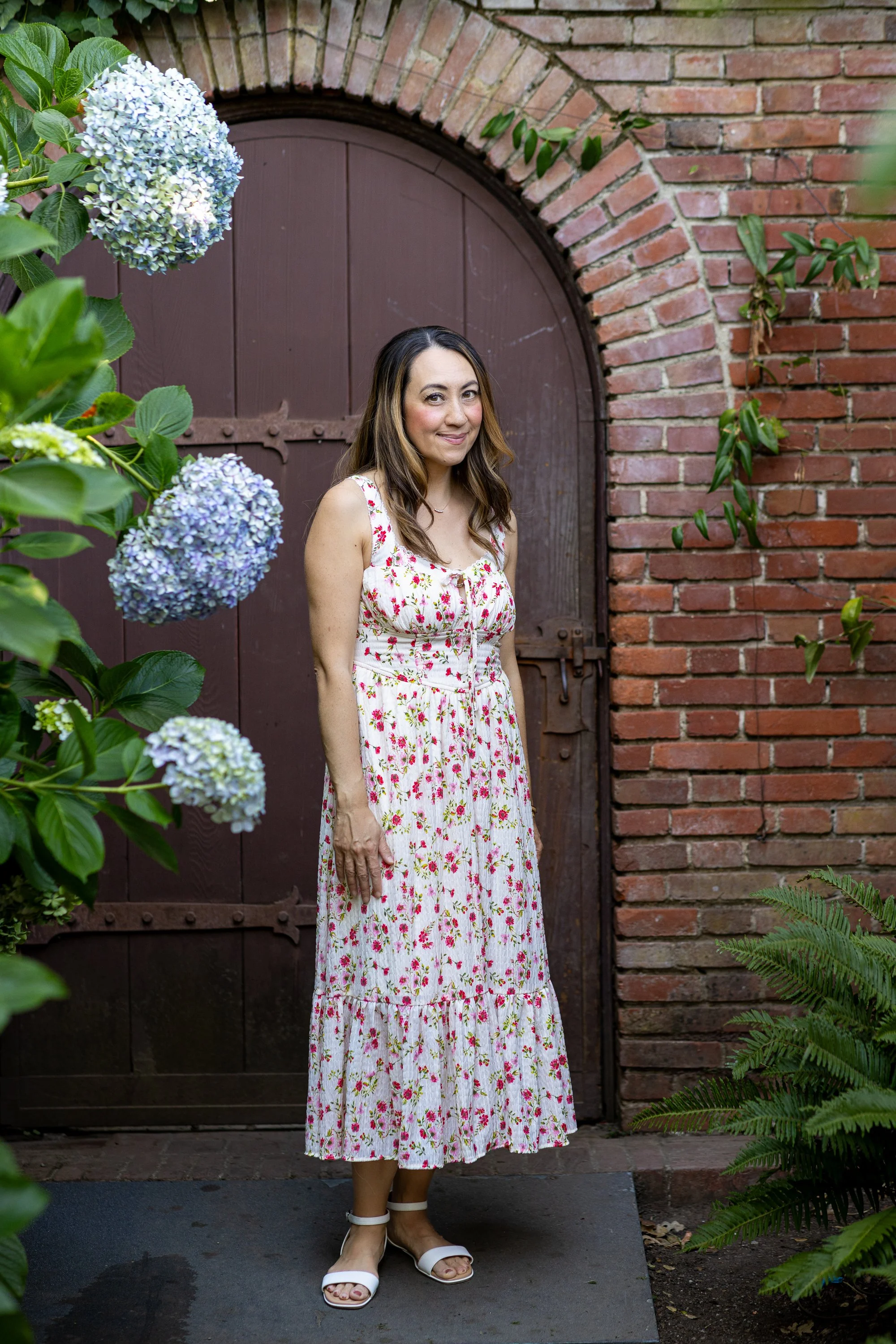 Woman in floral dress under brick arch beside blue hydrangeas at Filoli