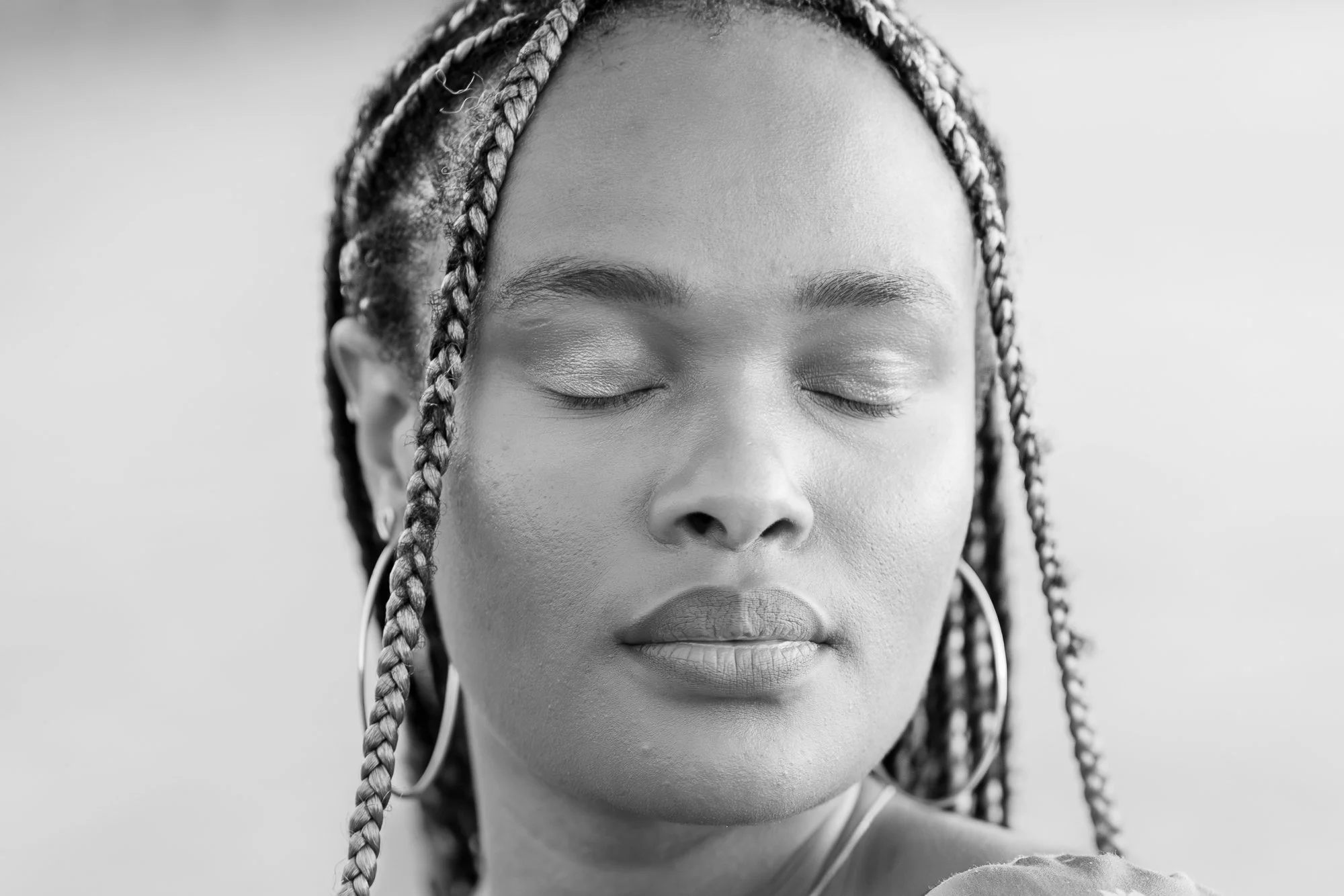 Black and white close-up of woman with braided hair, closed eyes, hoop earrings, and wearing earphones.