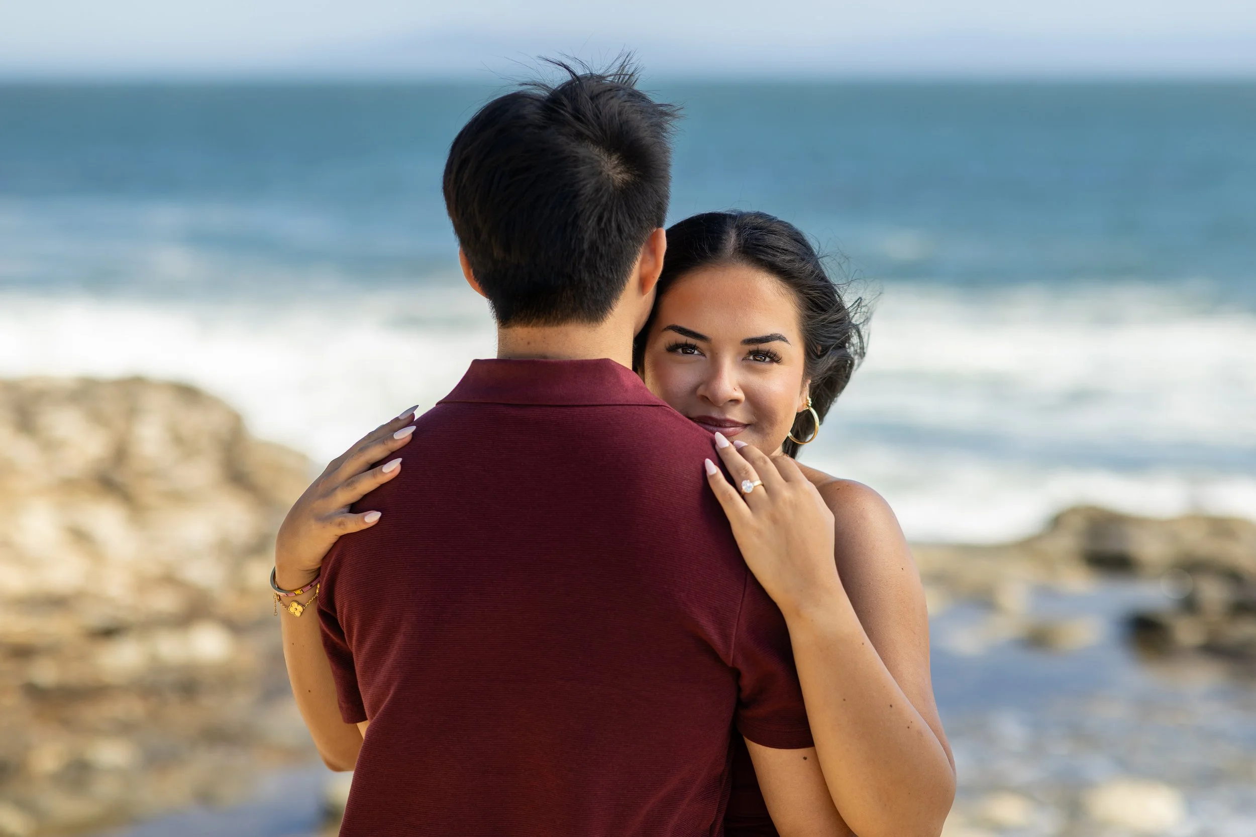 Woman smiling over her fiancé's shoulder with the Santa Cruz coastline behind them