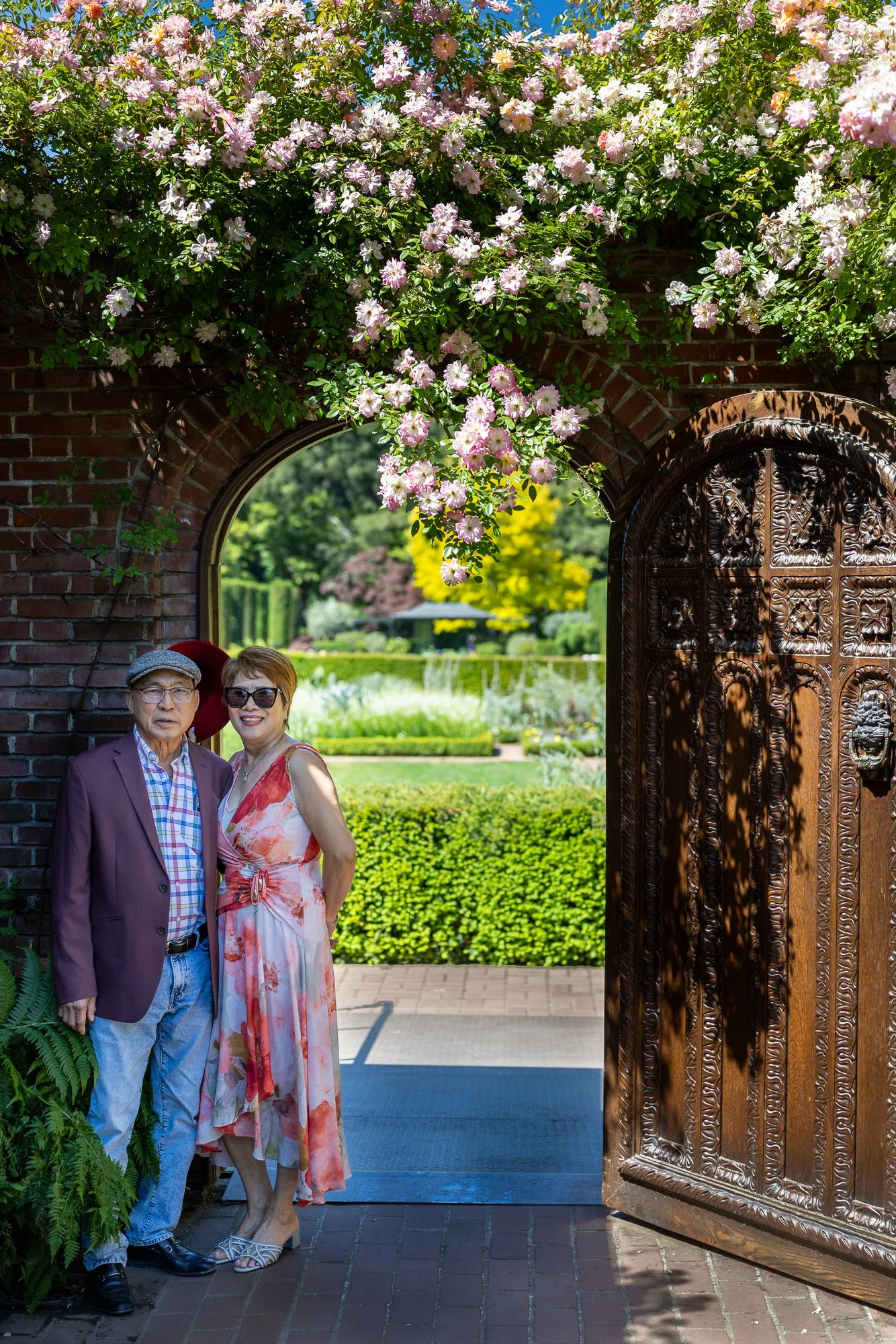 Older couple under climbing rose arch and carved gate at Filoli Gardens, Woodside spring portrait