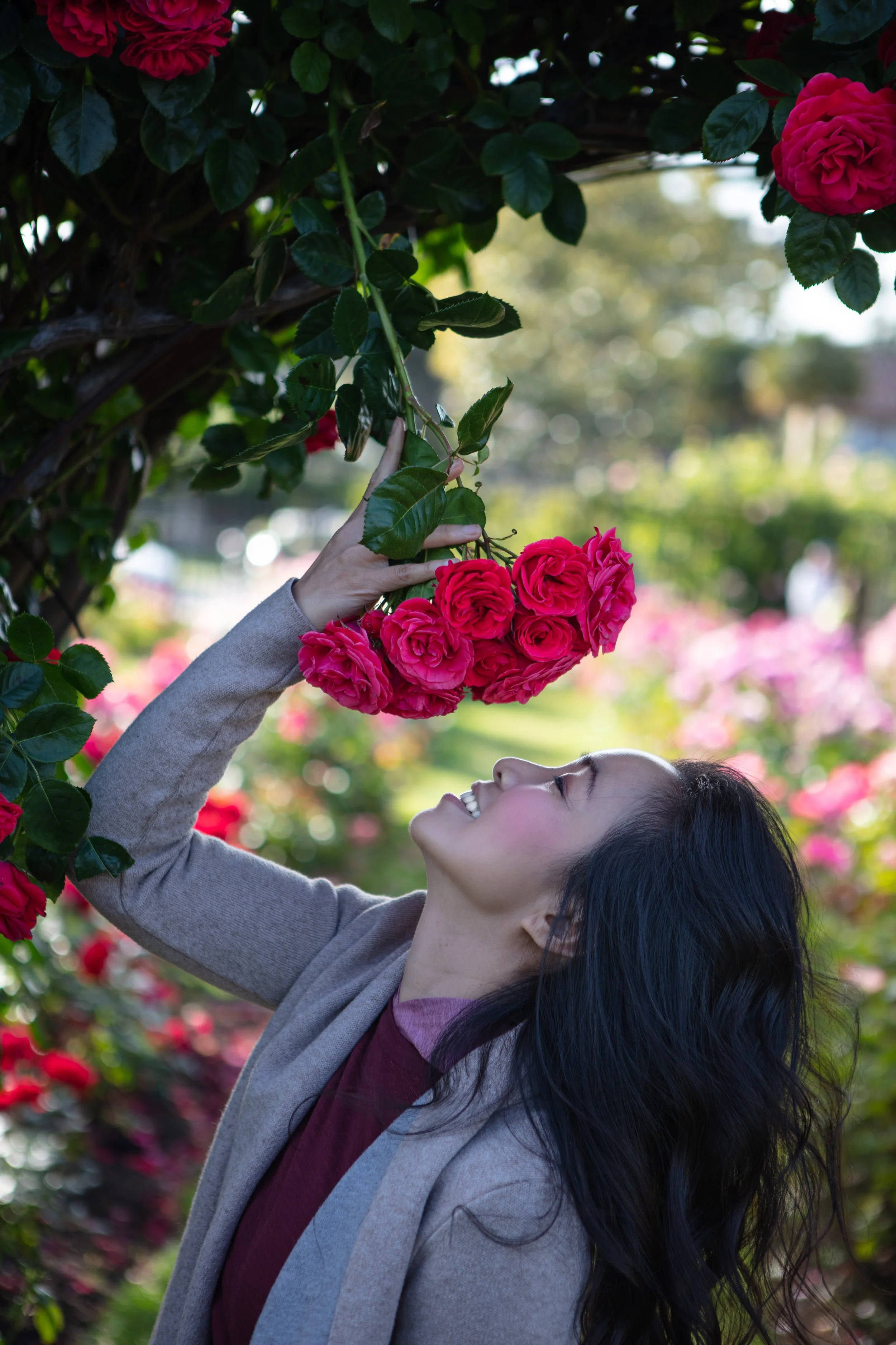 A woman smiling and holding a bunch of pink roses in a garden.