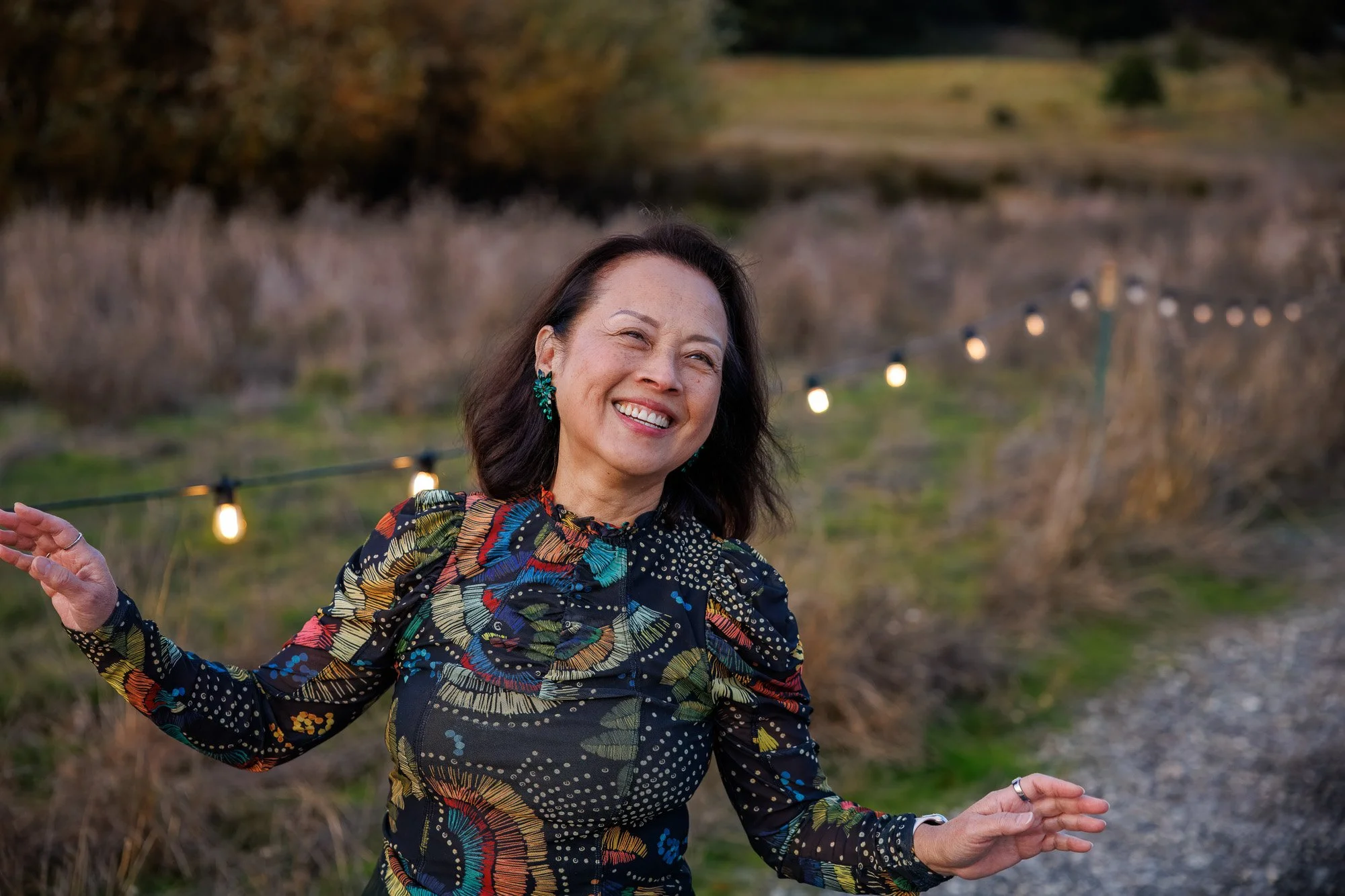 Woman in colorful dress with arms outstretched laughing on garden path with string lights at Filoli Historic Garden Woodside California