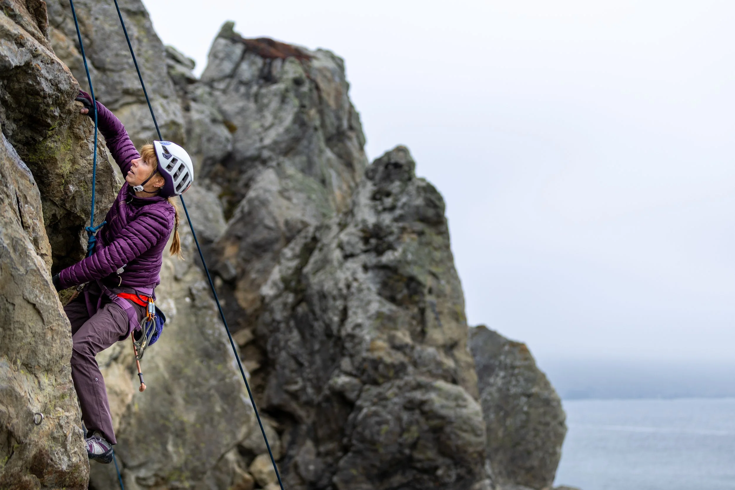 Mickey's Beach Rock climbing action photo by matthew duncan - woman in puple jacket over water