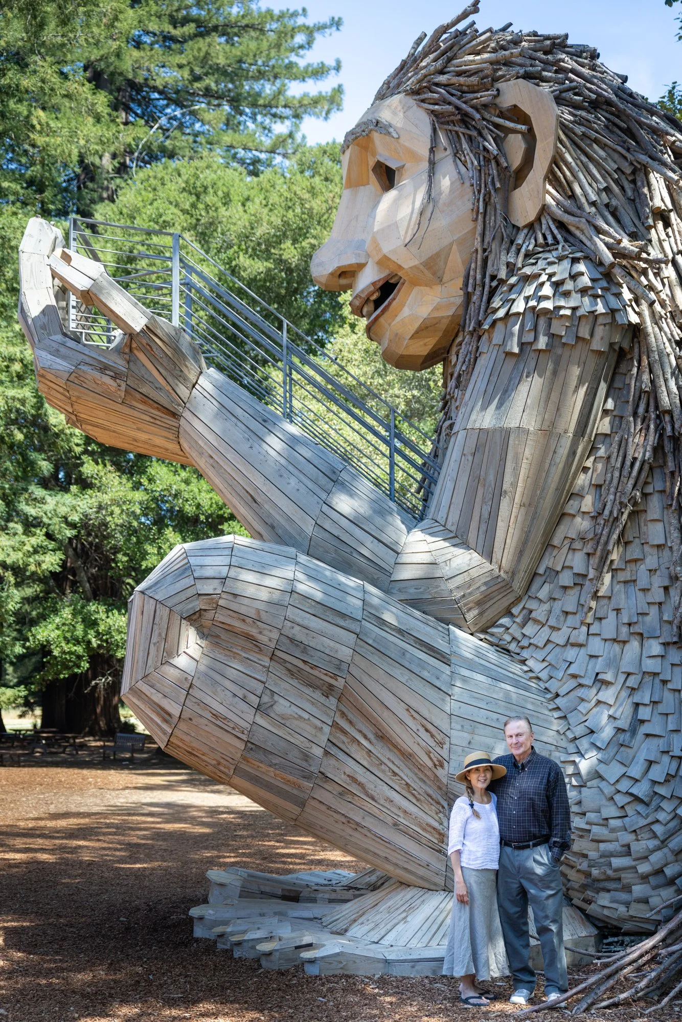 Couple beneath a giant Thomas Dambo reclaimed-wood troll sculpture in Filoli's natural lands, Woodside