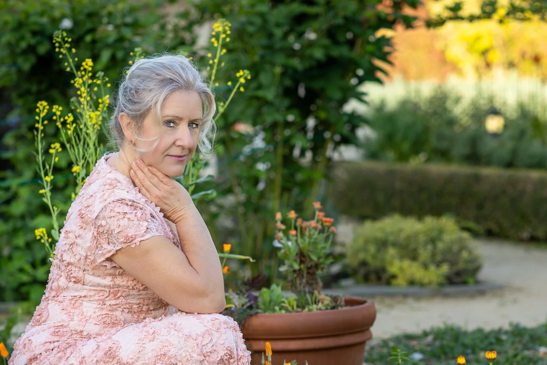 Woman in blush pink dress with hand near jaw, relaxed candid portrait in garden setting with golden morning light, Bay Area personal lifestyle photography