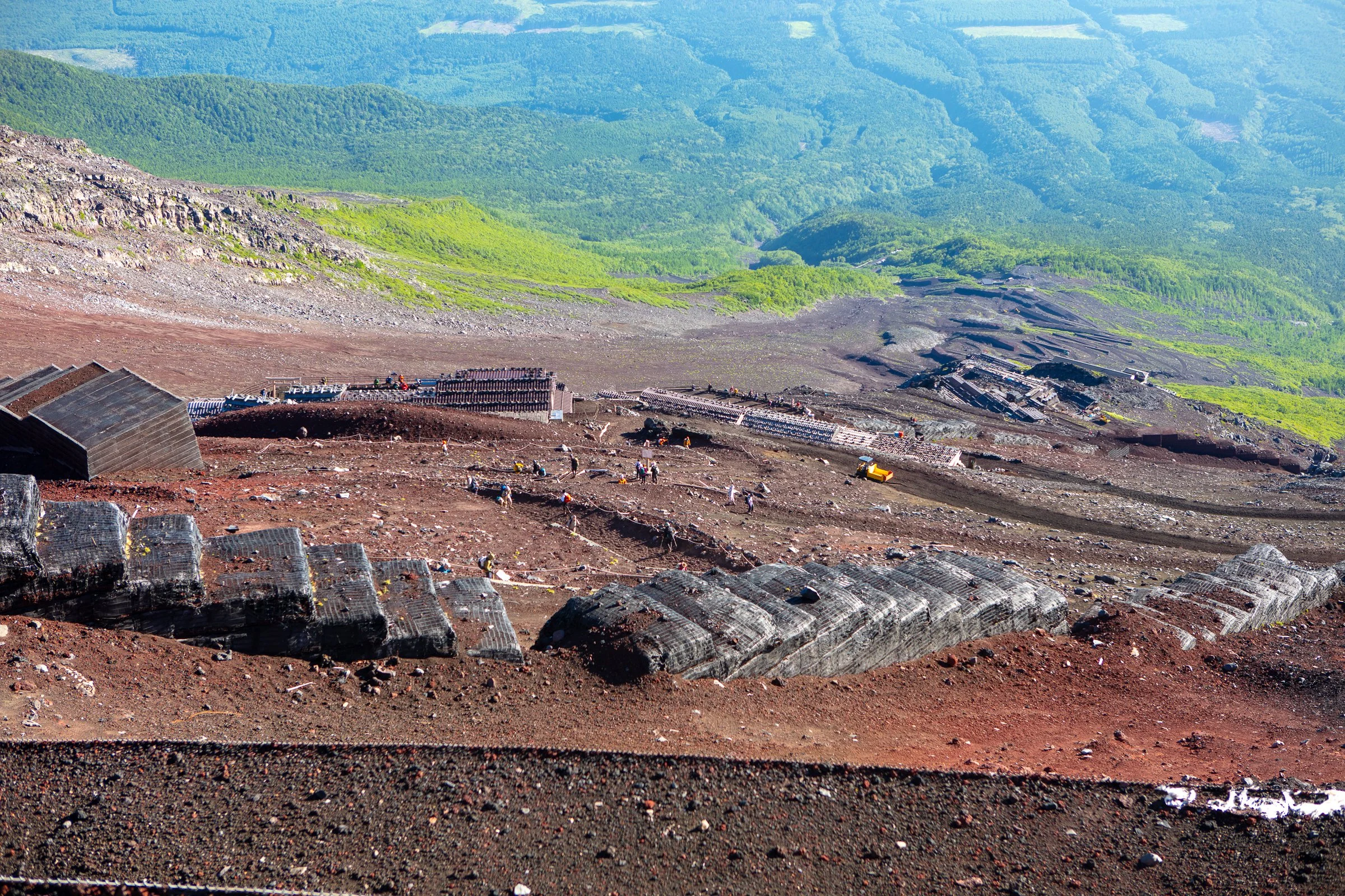 Looking down Mt Fuji volcanic scree trail hikers below green forest Japan