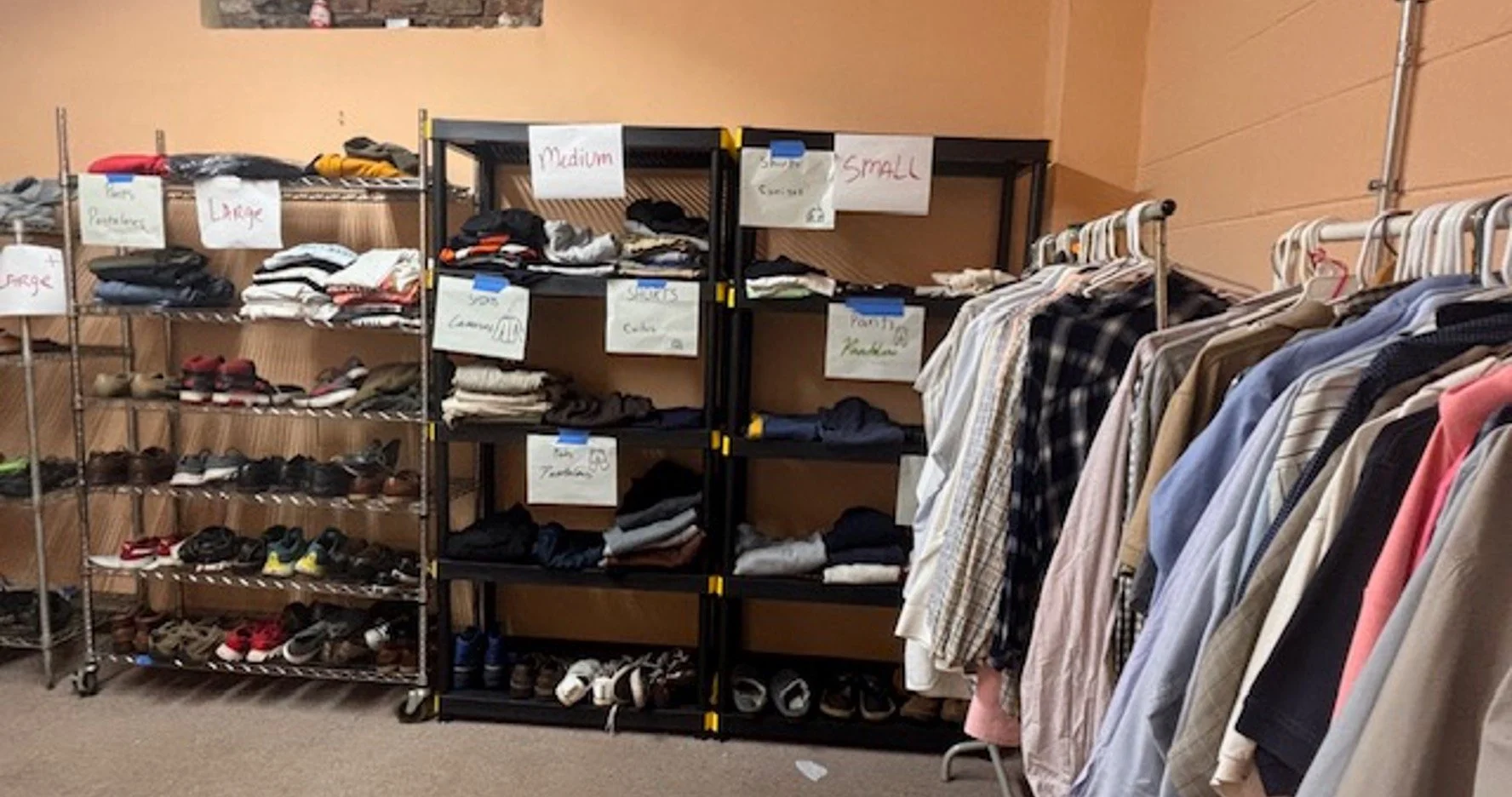Shelves and racks filled with clothing, shoes, and accessories at a sales or donation event, organized by size labels like large, medium, small, and extra large.