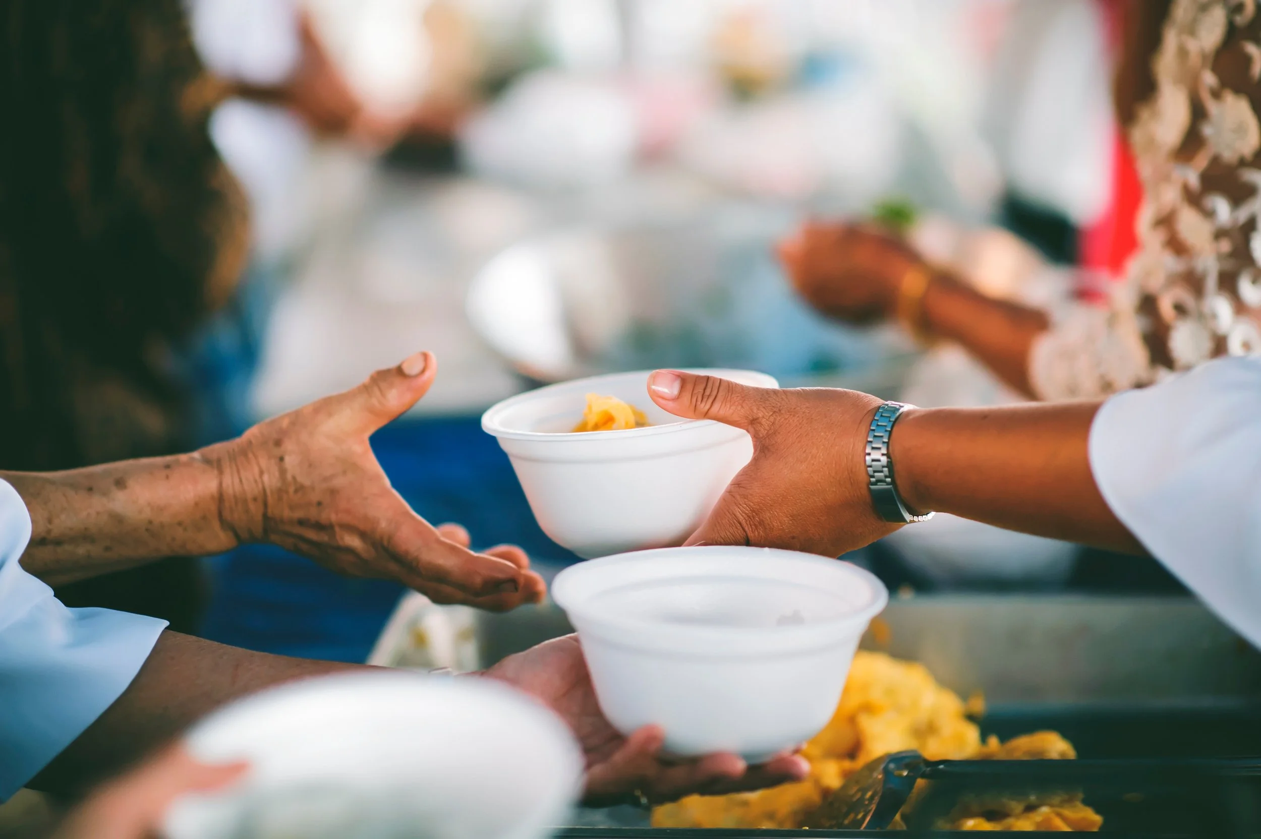 People distributing food in styrofoam bowls at a community service event.