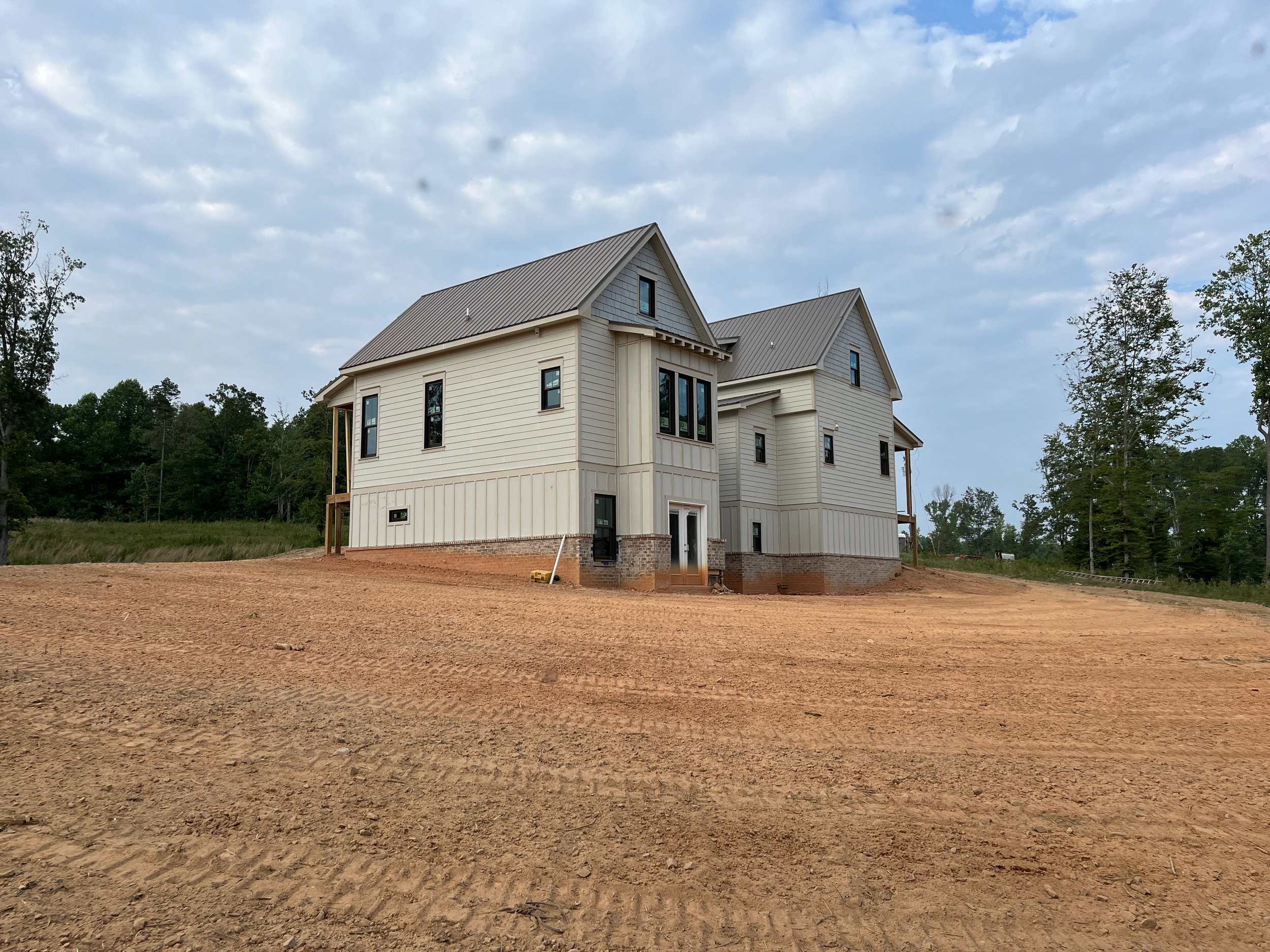 Newly constructed house on a dirt lot with green trees in the background.