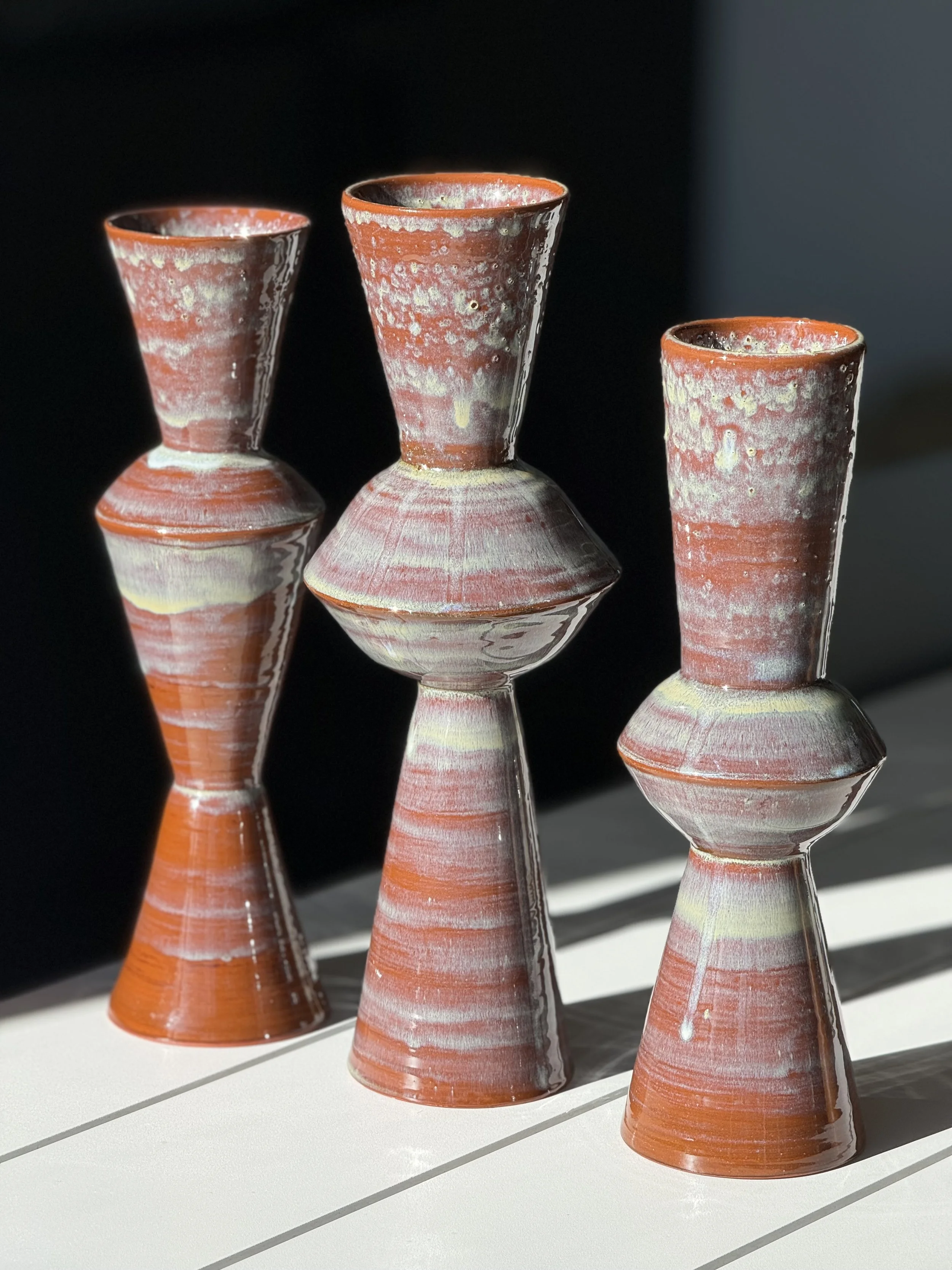 Three ceramic vases with reddish-orange and cream colored glaze varying in heights and widths.