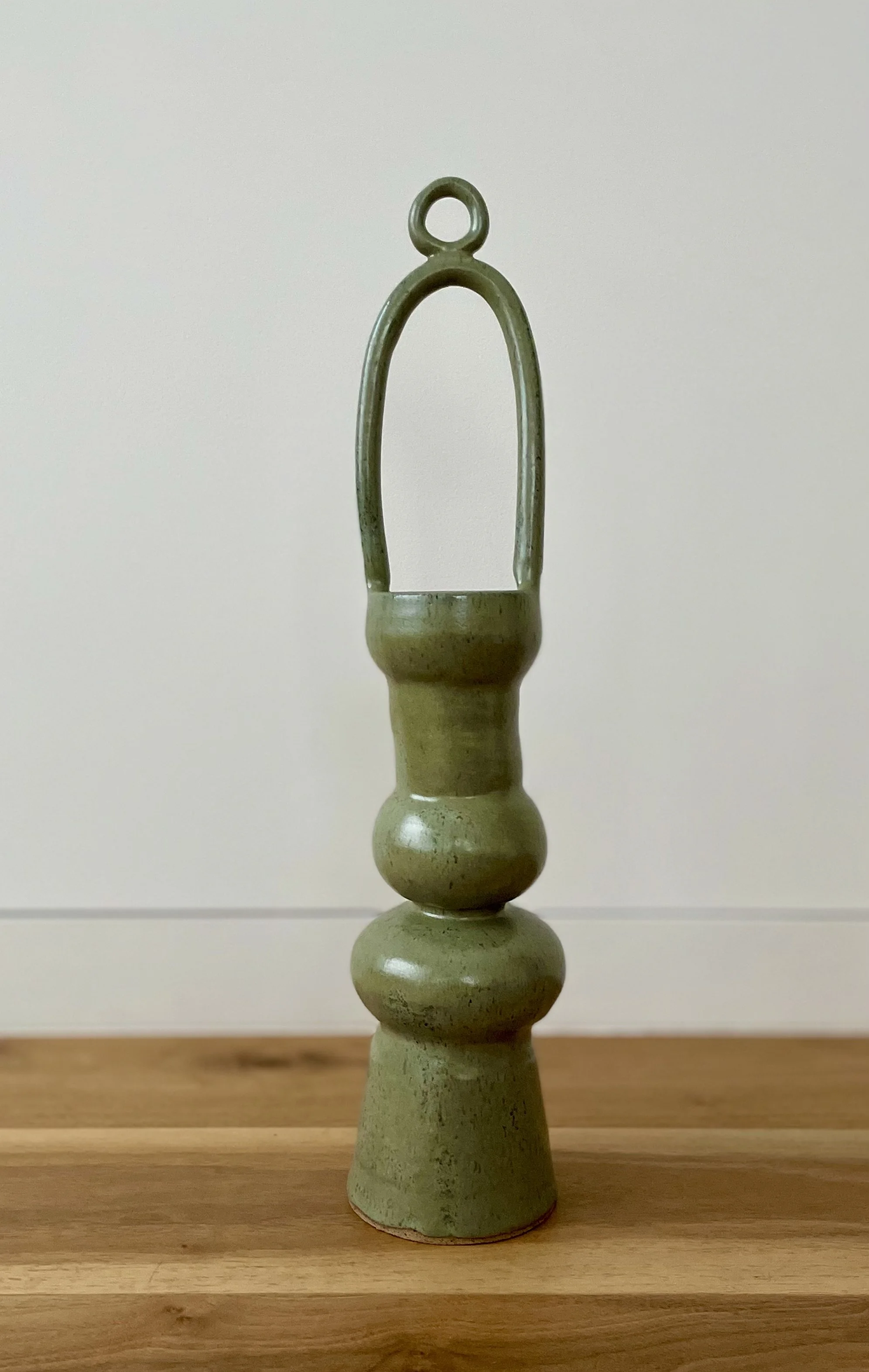 A green ceramic geometric sculpture with a tall loop handle.