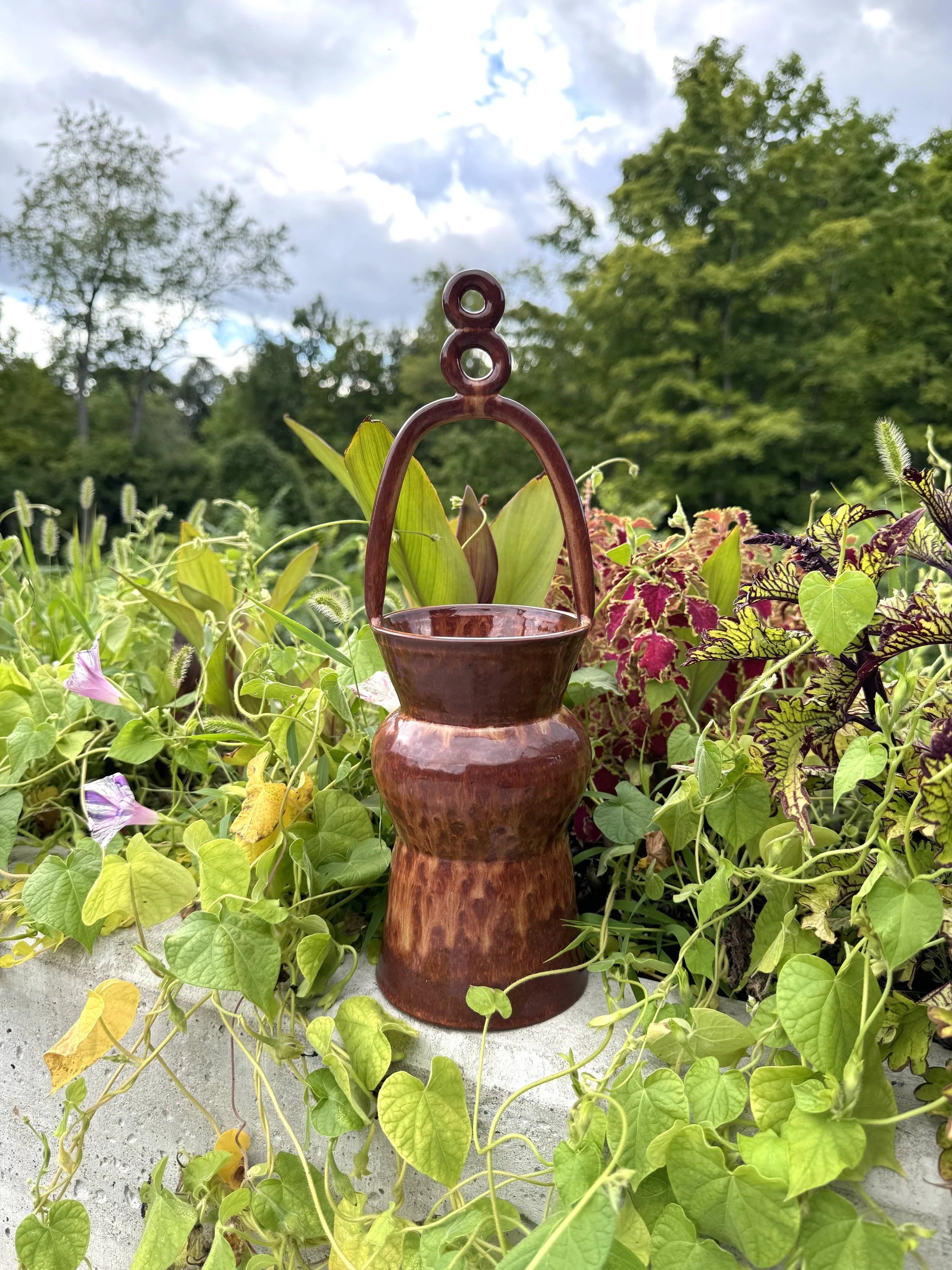 A brown ceramic sculpture with a tall looped handle.