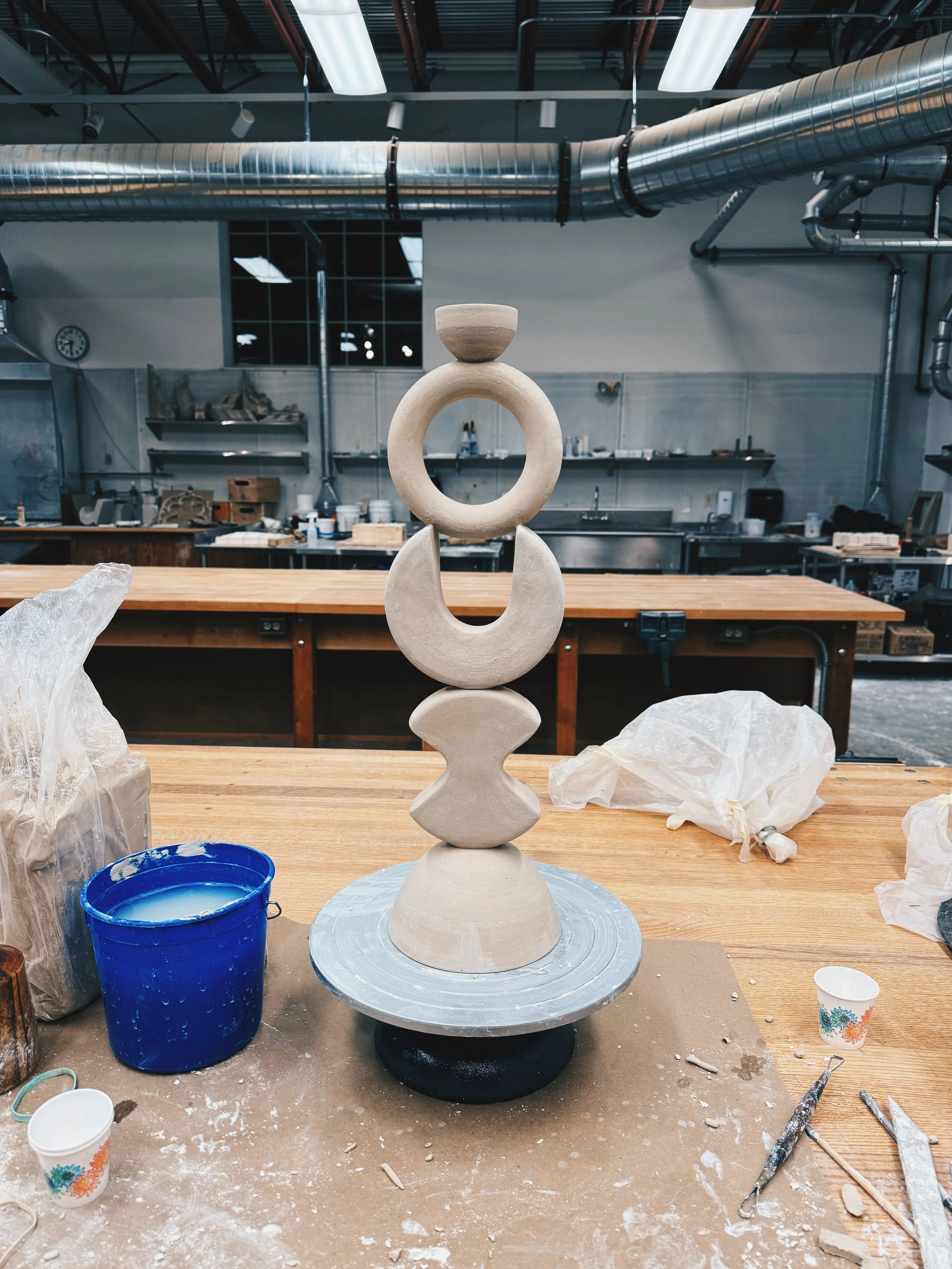A tall geometric ceramic sculpture in progress in a studio.