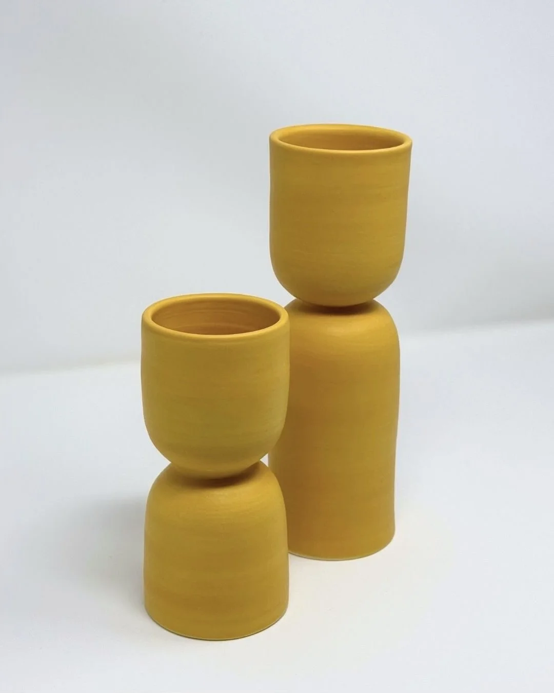 Two matte yellow ceramic sculptural cups and vases.