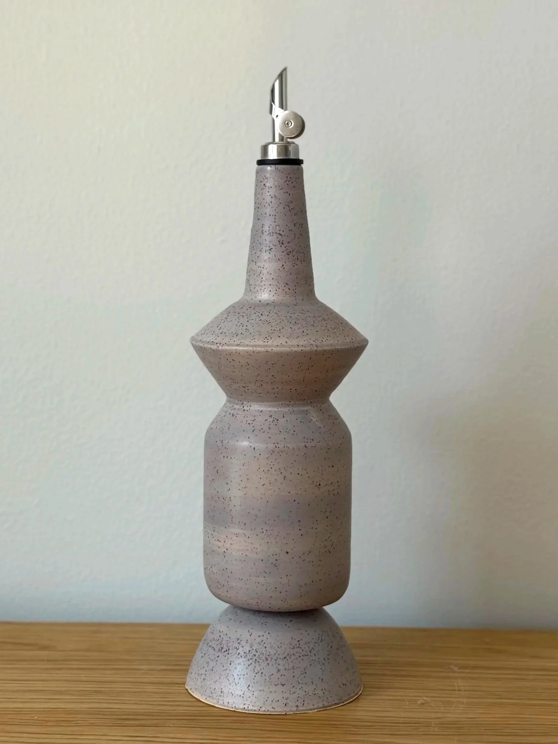 A sculptural geometric light gray ceramic olive oil dispenser.