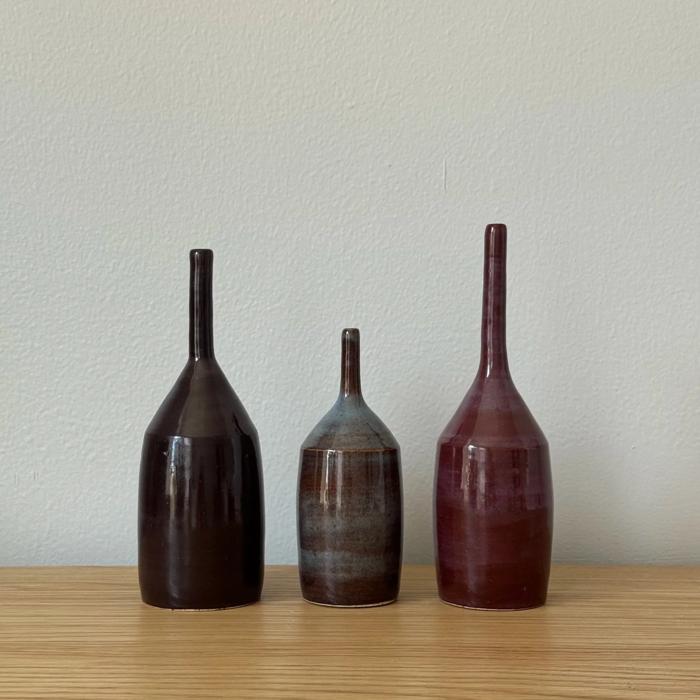 Three ceramic bottles with long, narrow necks and rounded bases.