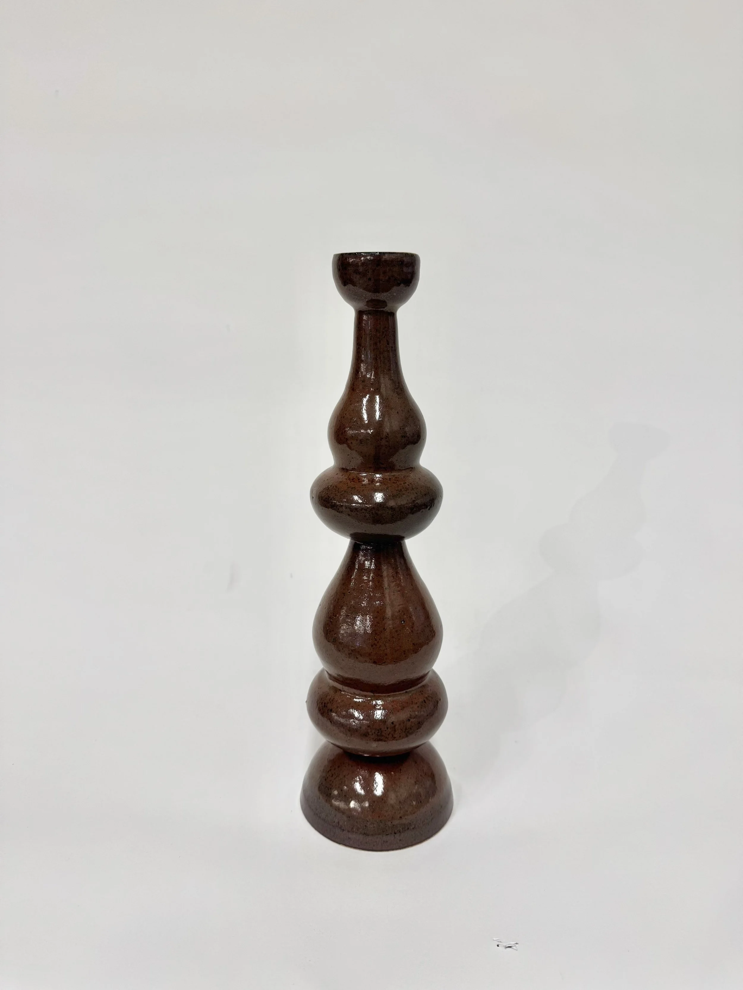 A brown, symmetric ceramic sculpture with a curvy, tiered design standing on a white surface against a white background.