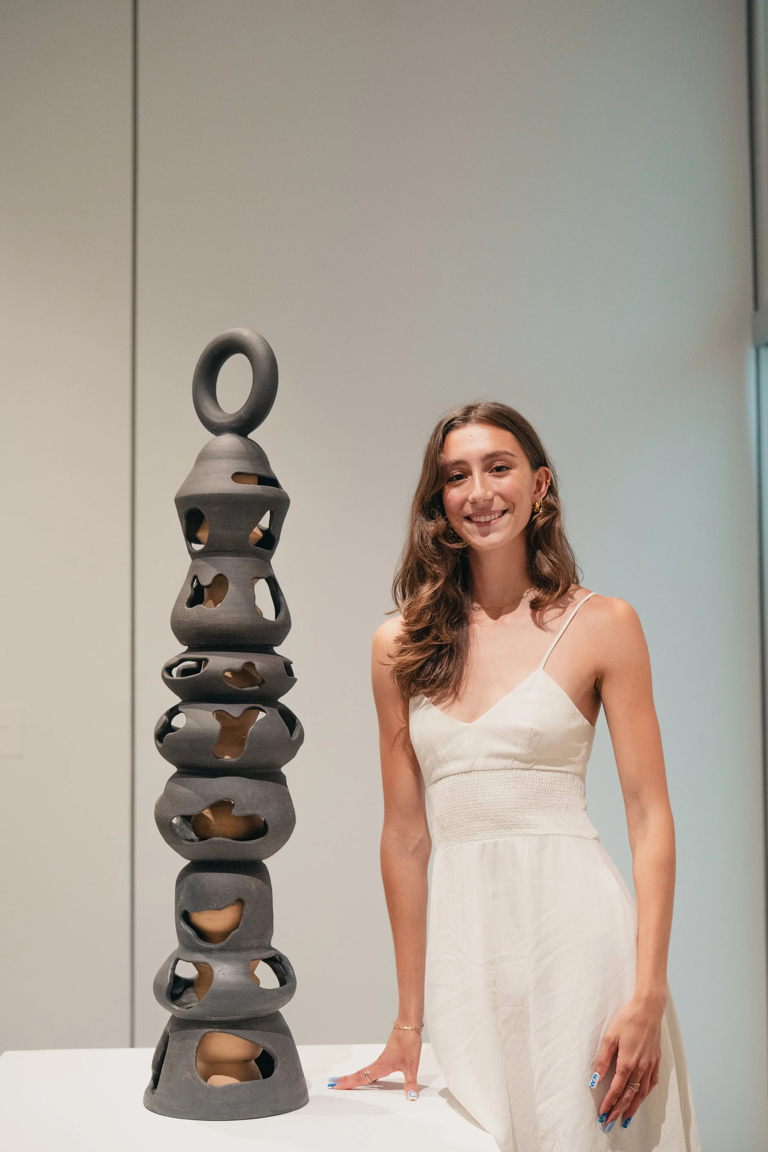 Fiona Mejico standing next to her senior capstone exhibition work, a 4 foot tall ceramic sculpture .