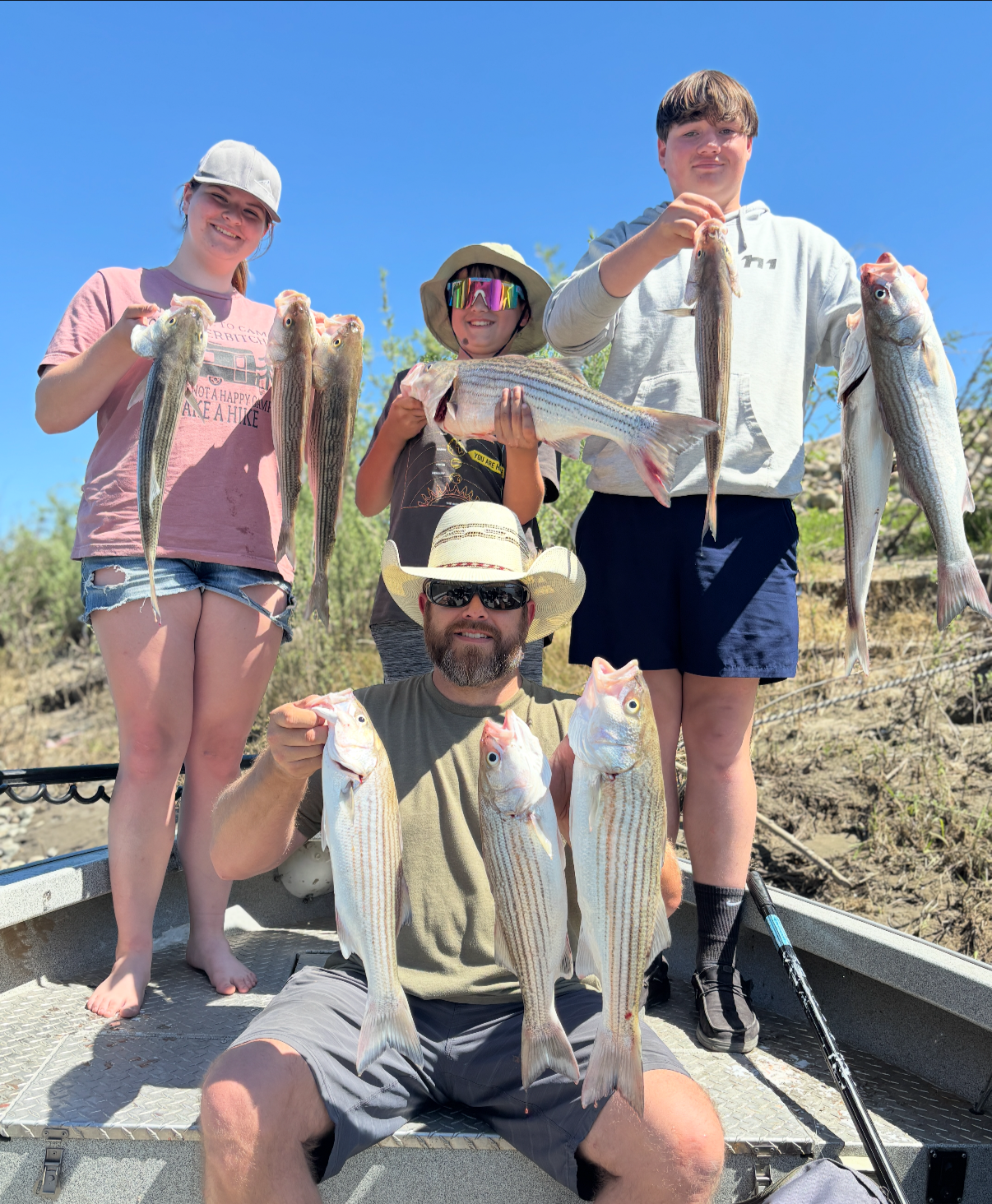 Group of five people on a boat displaying freshly caught fish, outdoors on a sunny day.