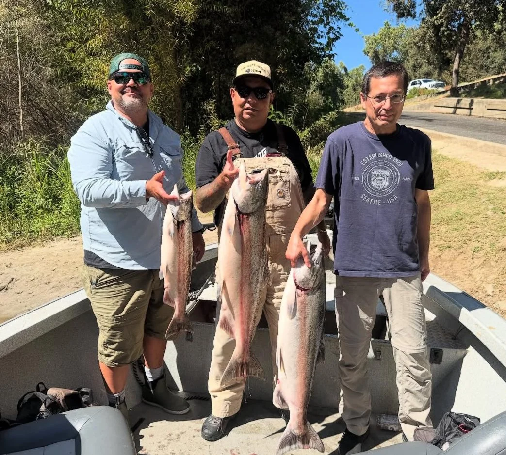 Three men standing on a boat outdoors holding large fish they caught.