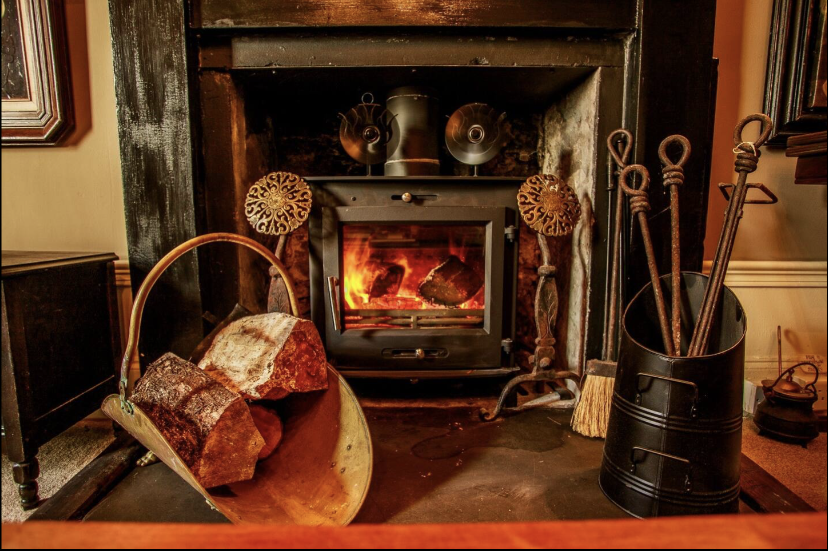 Fireplace with burning logs, surrounded by fireplace tools and decorative items, in a cozy room.