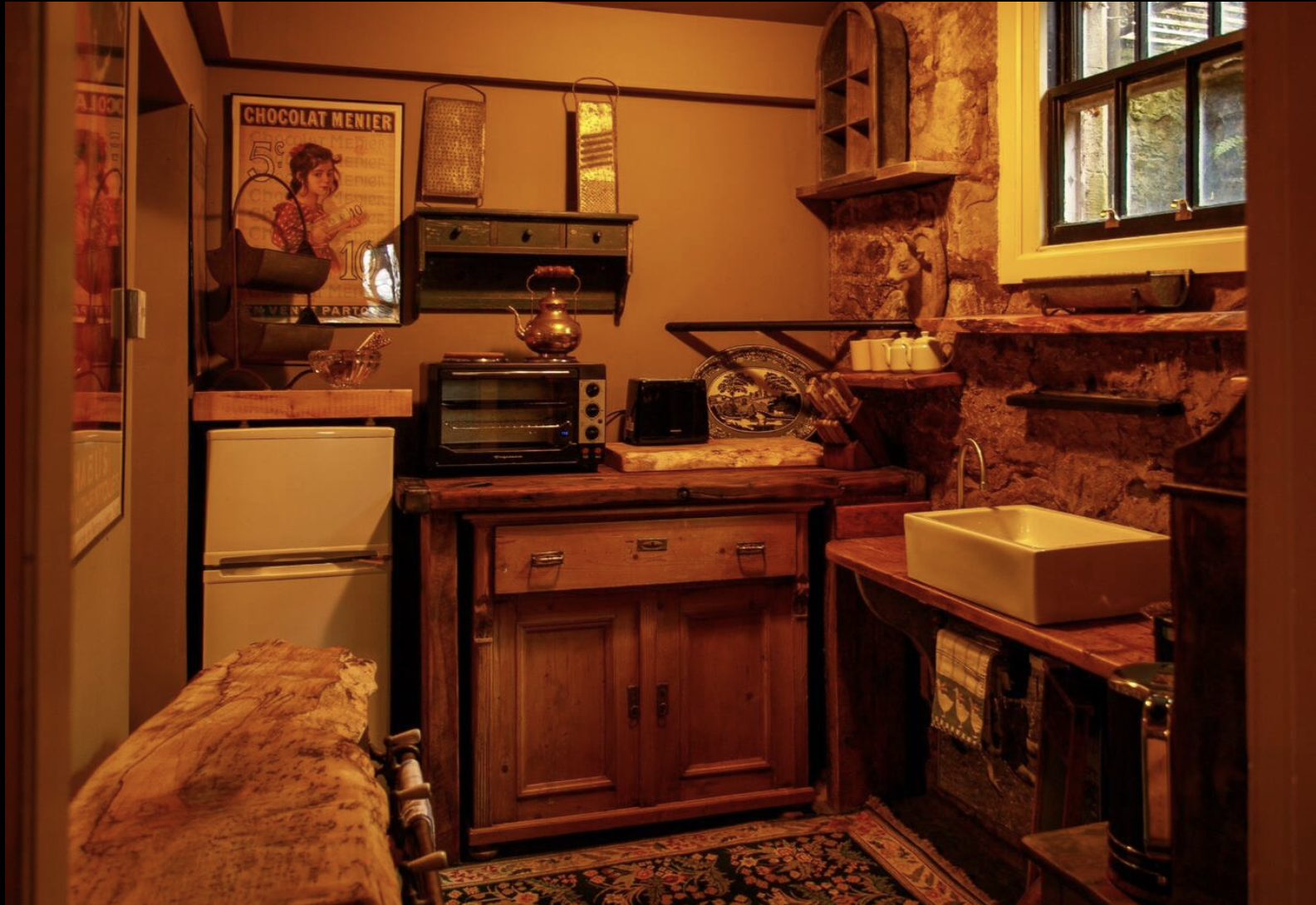 Cozy rustic kitchen with stone walls, wooden cabinetry, vintage appliances, and shelves with dishes.