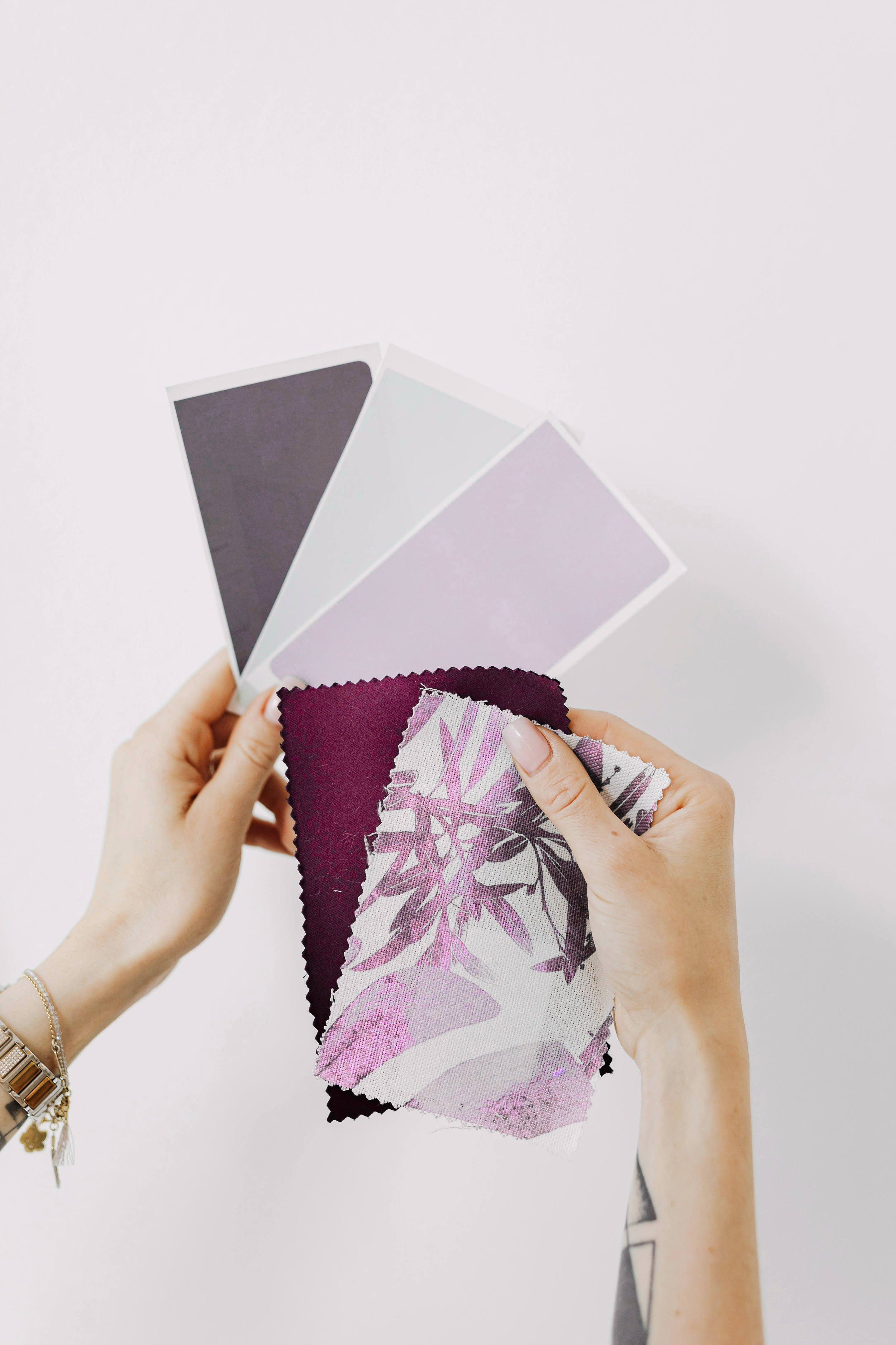 Hands holding fabric swatches and color samples against a plain white background.
