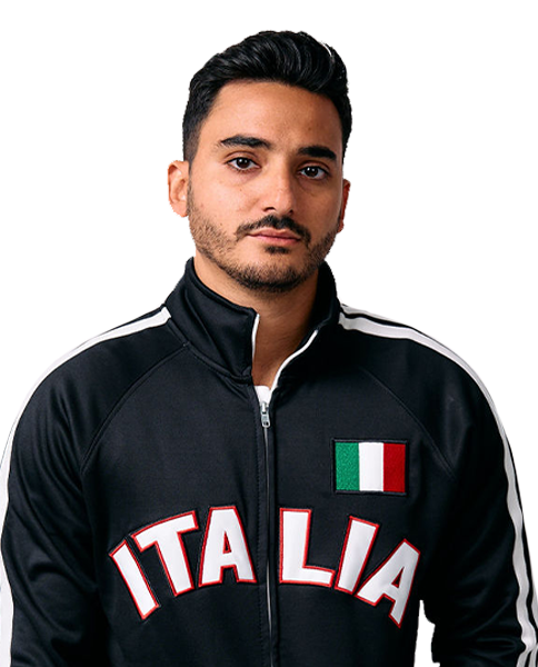 A young man with dark hair and facial hair wearing a black tracksuit with white stripes on the shoulders, and Italian flag and Italy text on the front.