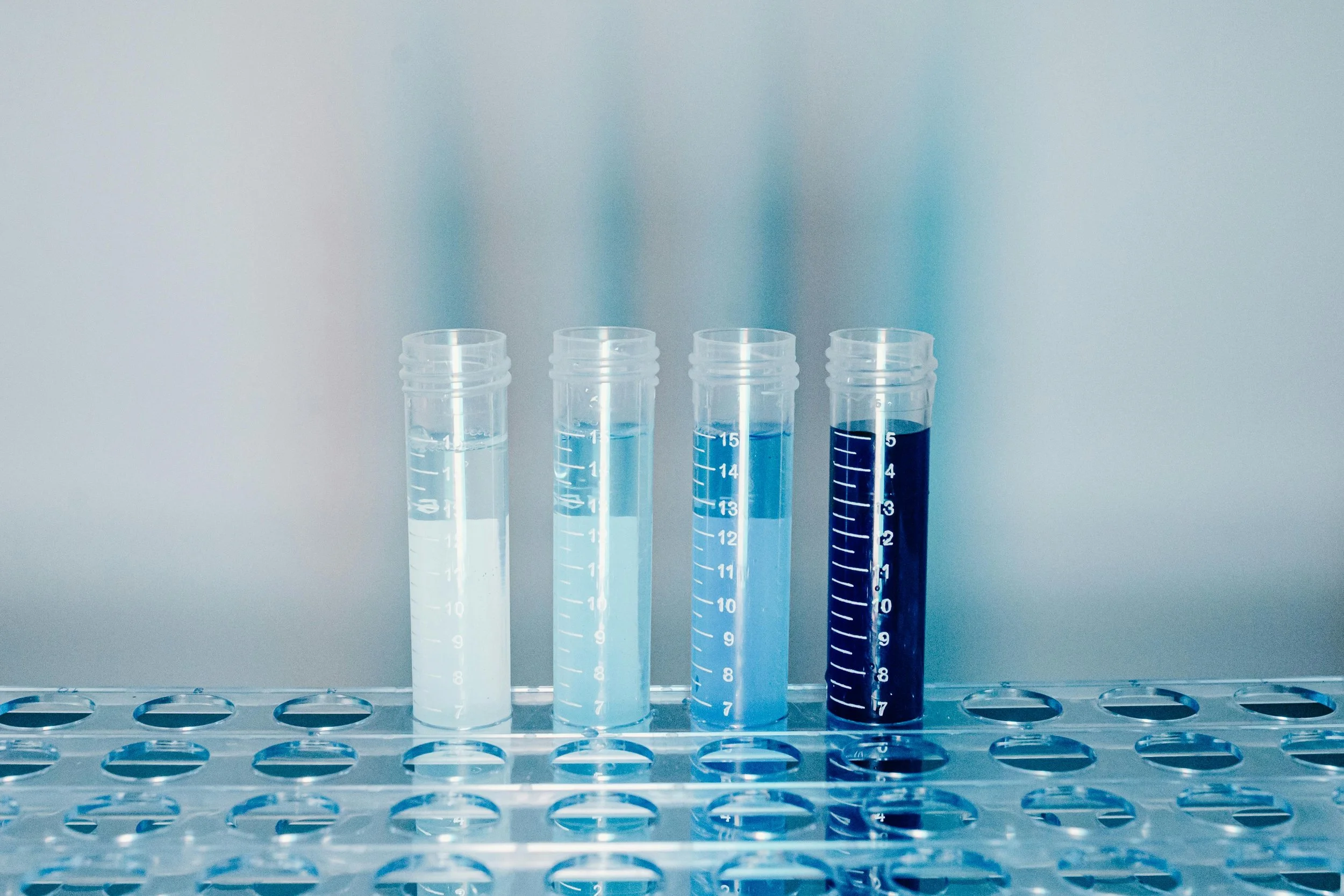 Four test tubes filled with liquids of varying shades of blue, placed in a rack against a plain background.