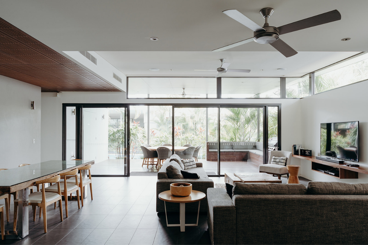 Living room with large sliding glass doors leading to an outdoor patio, featuring a dining table, chairs, and a seating area with sofas, a TV, and ceiling fans.