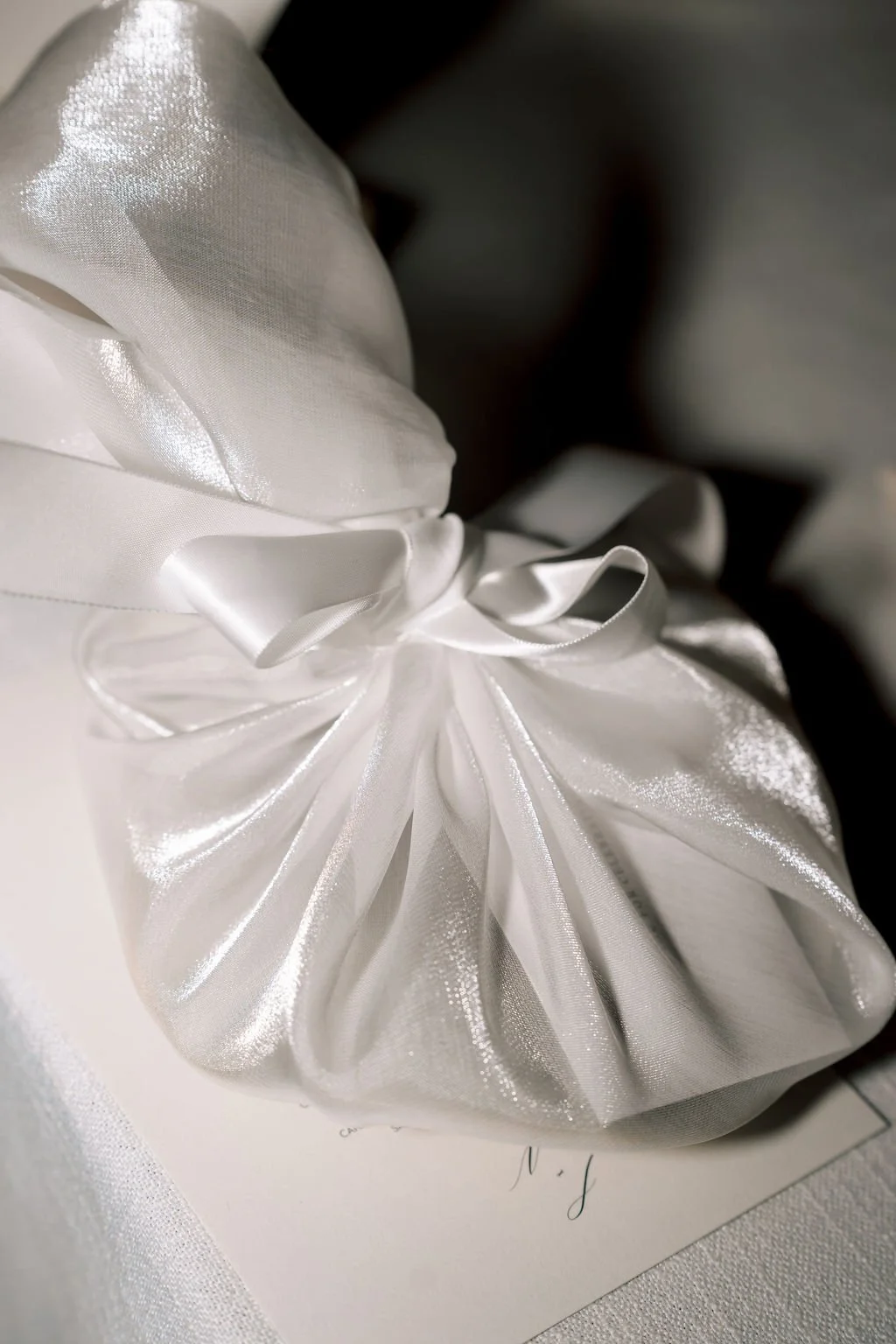 A white satin gift bag with a shiny finish, tied with a satin ribbon in a bow.