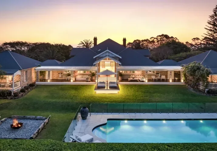 Luxury house with a backyard pool, fire pit, and well-maintained lawn during sunset.