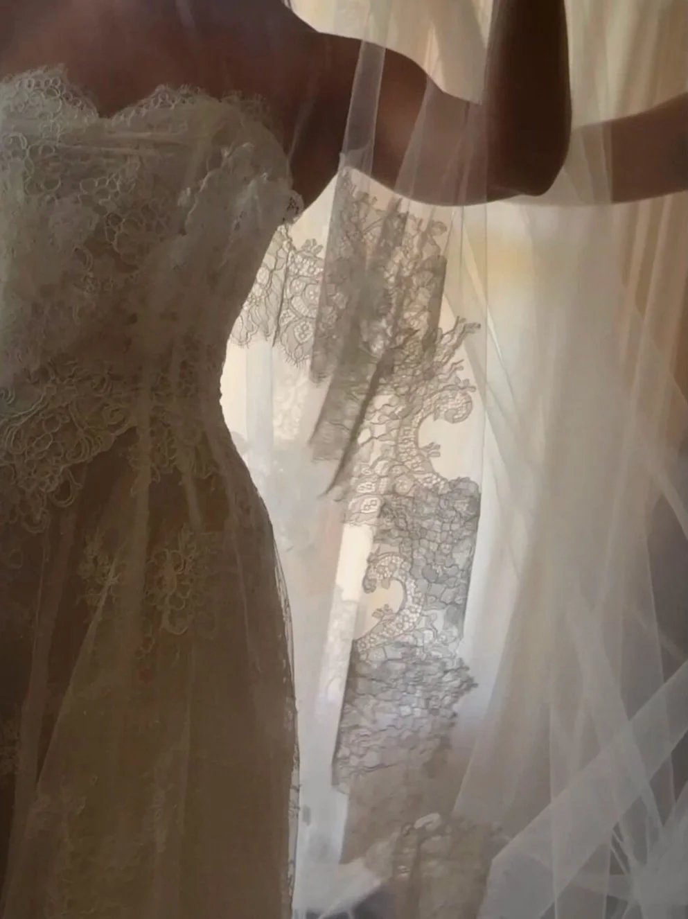 Close-up of a bride wearing a lace wedding dress, seen through a sheer veil.