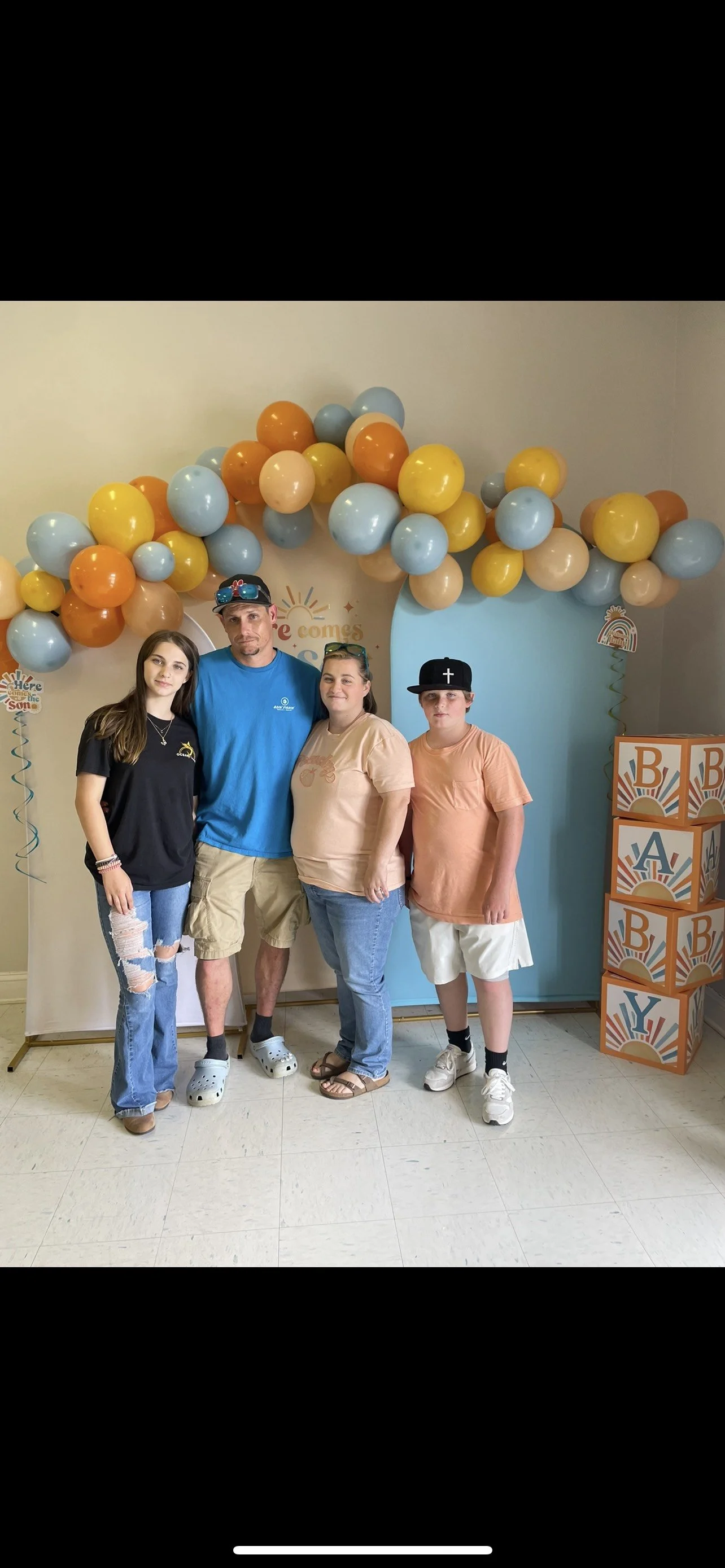 Four people standing in front of a colorful balloon arch and decorated backdrop at a celebration event
