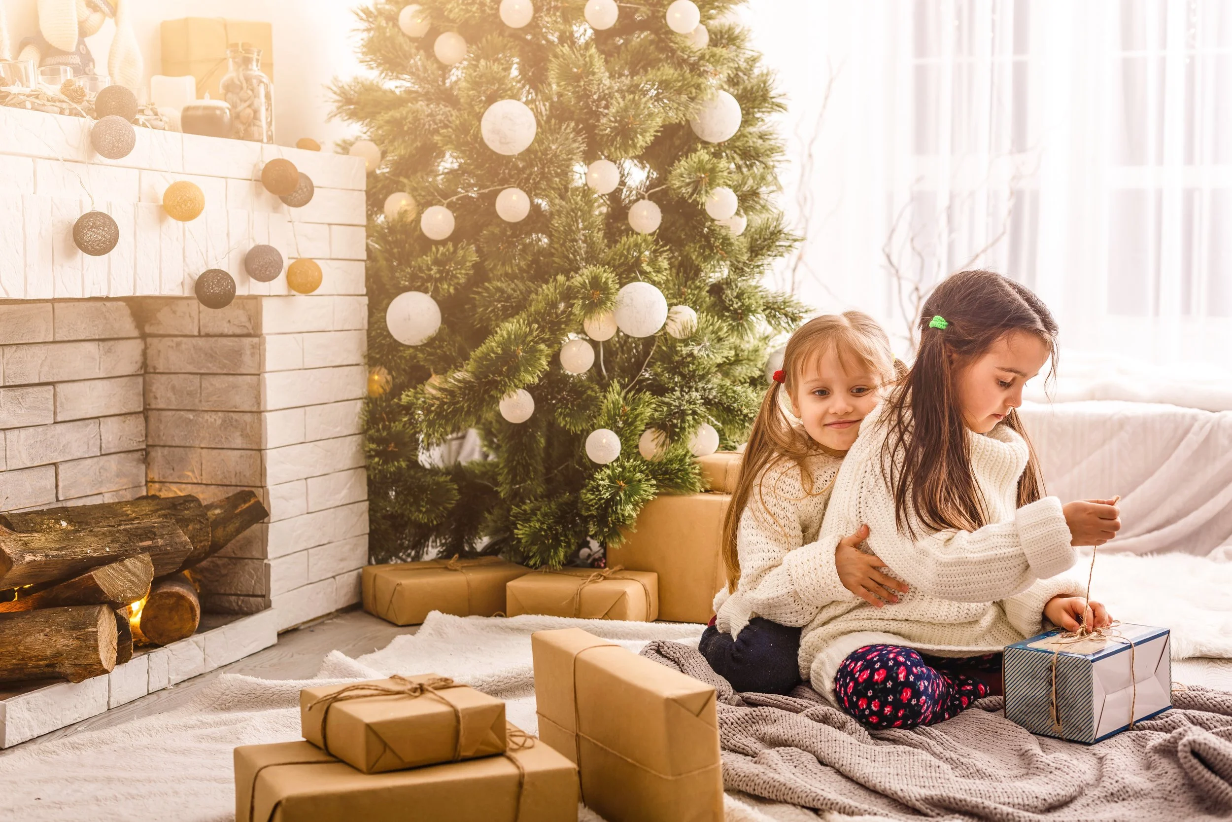 Two children opening Christmas gifts together beside a Christmas tree