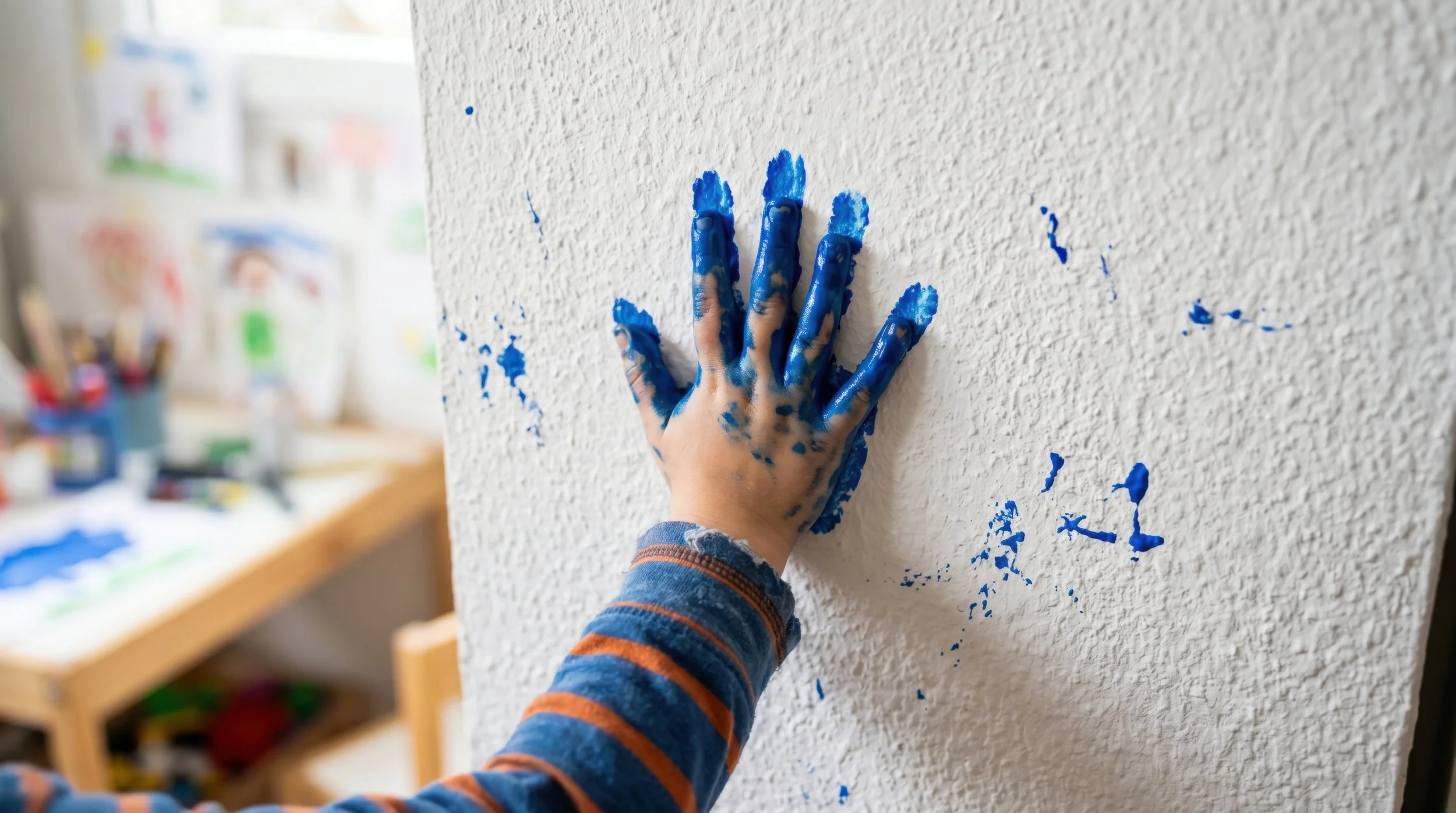 Child's hand covered in blue paint pressed onto a canvas, a handprint keepsake idea for Father's Day gifts