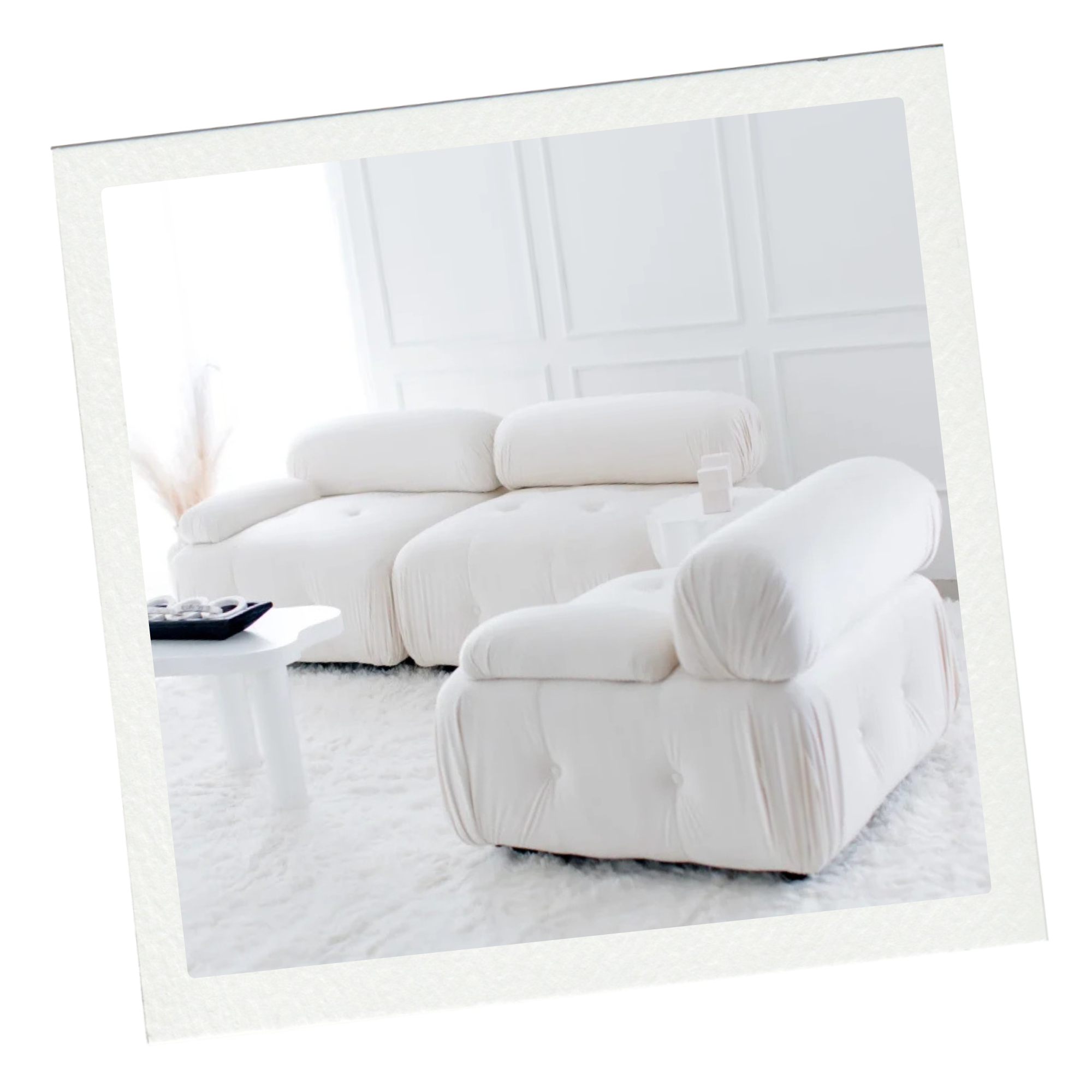 Bright living room with white sofa, armchair, and plush white rug, illuminated by natural light through large windows.