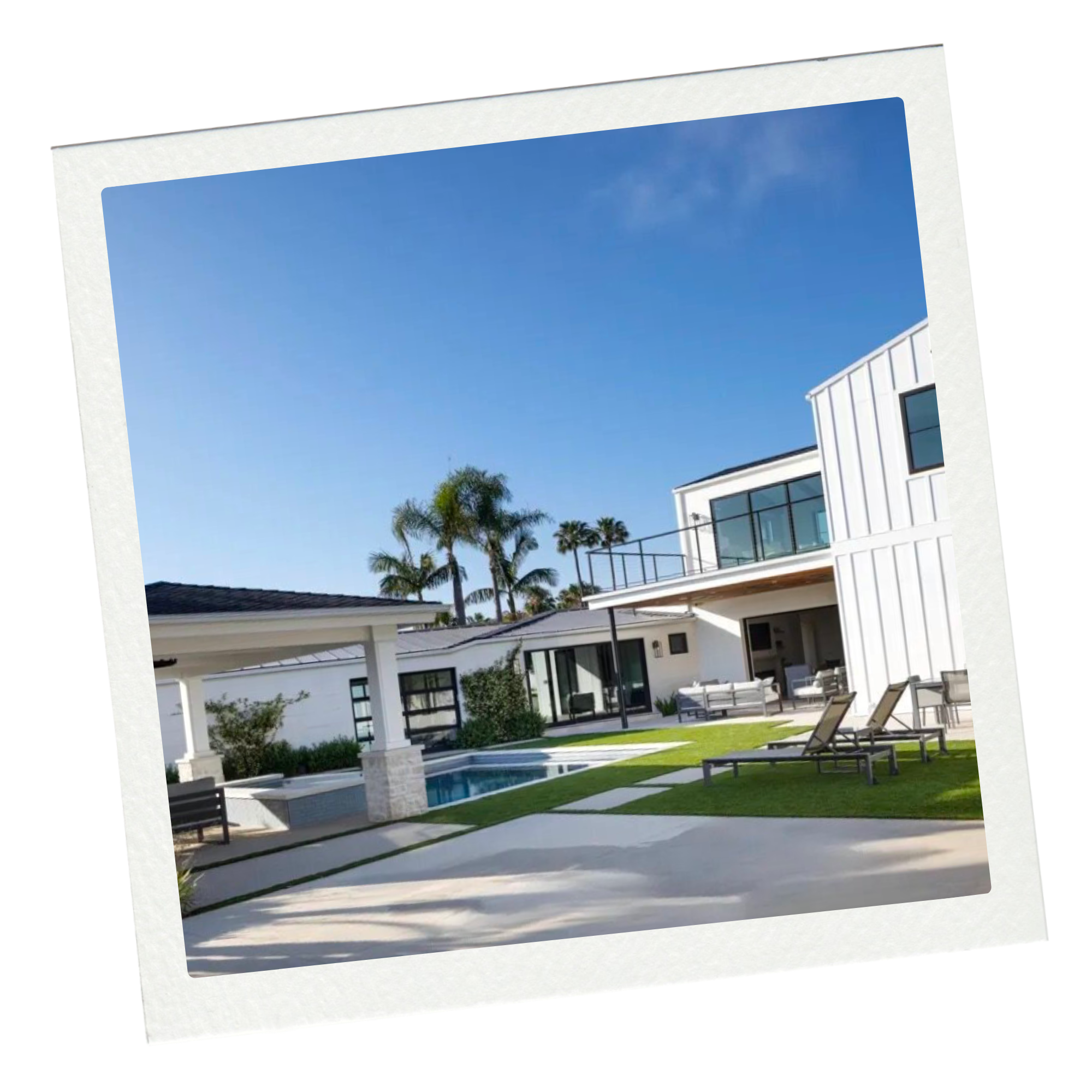 Modern white house with outdoor pool, lounge chairs, and patio furniture, palm trees in the background, clear blue sky.