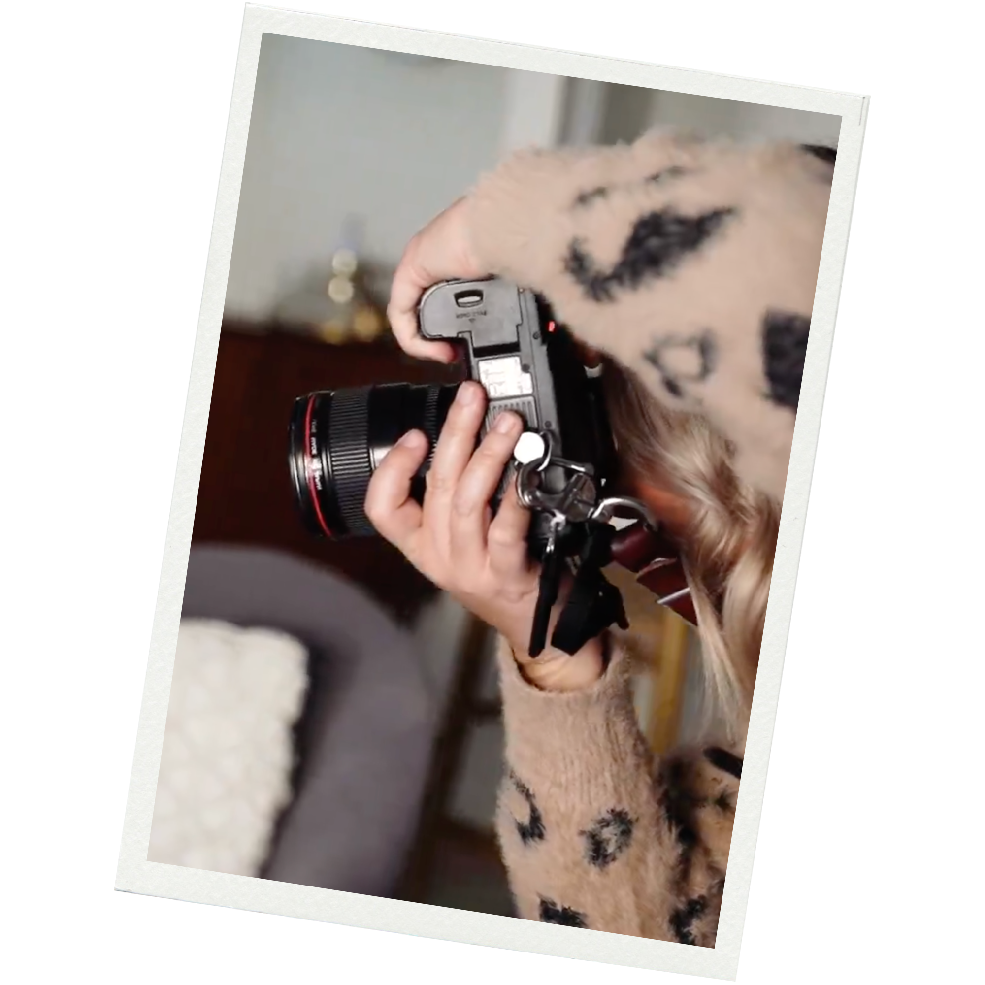 Person with long blonde hair taking a photograph with a digital camera indoors.