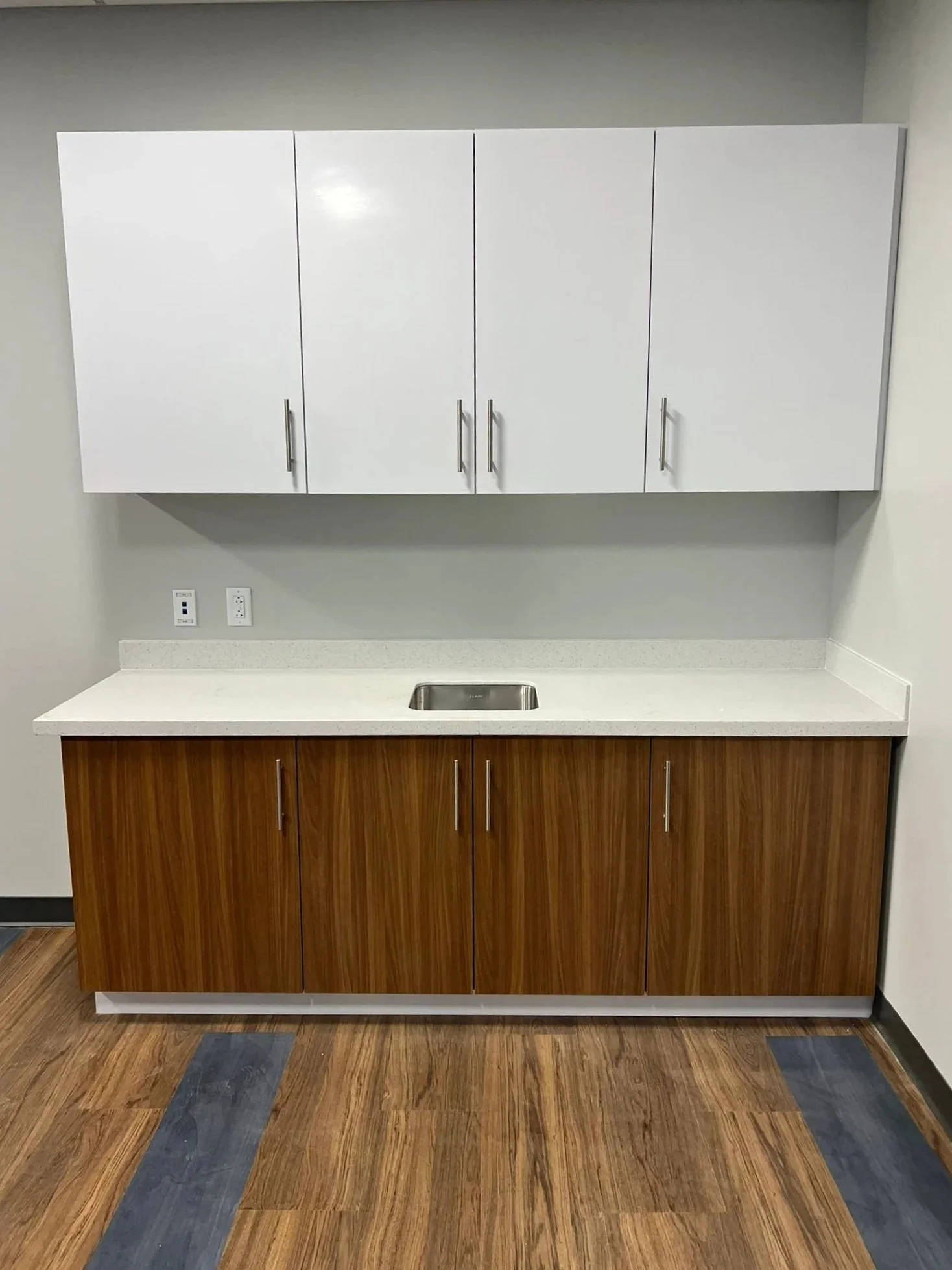 Kitchen cabinet with upper white doors and lower woodgrain doors, a countertop with a sink, and a wood floor with some darker gray patches.