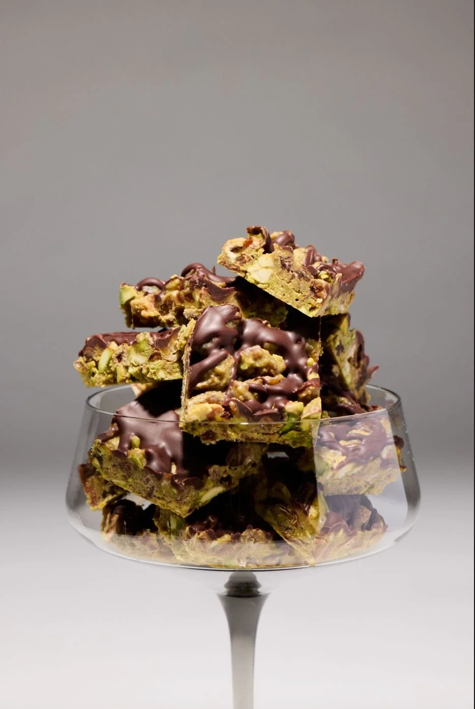 Stacked pistachio chocolate melt-in-your-mouth cookie bars in a clear glass dessert dish.