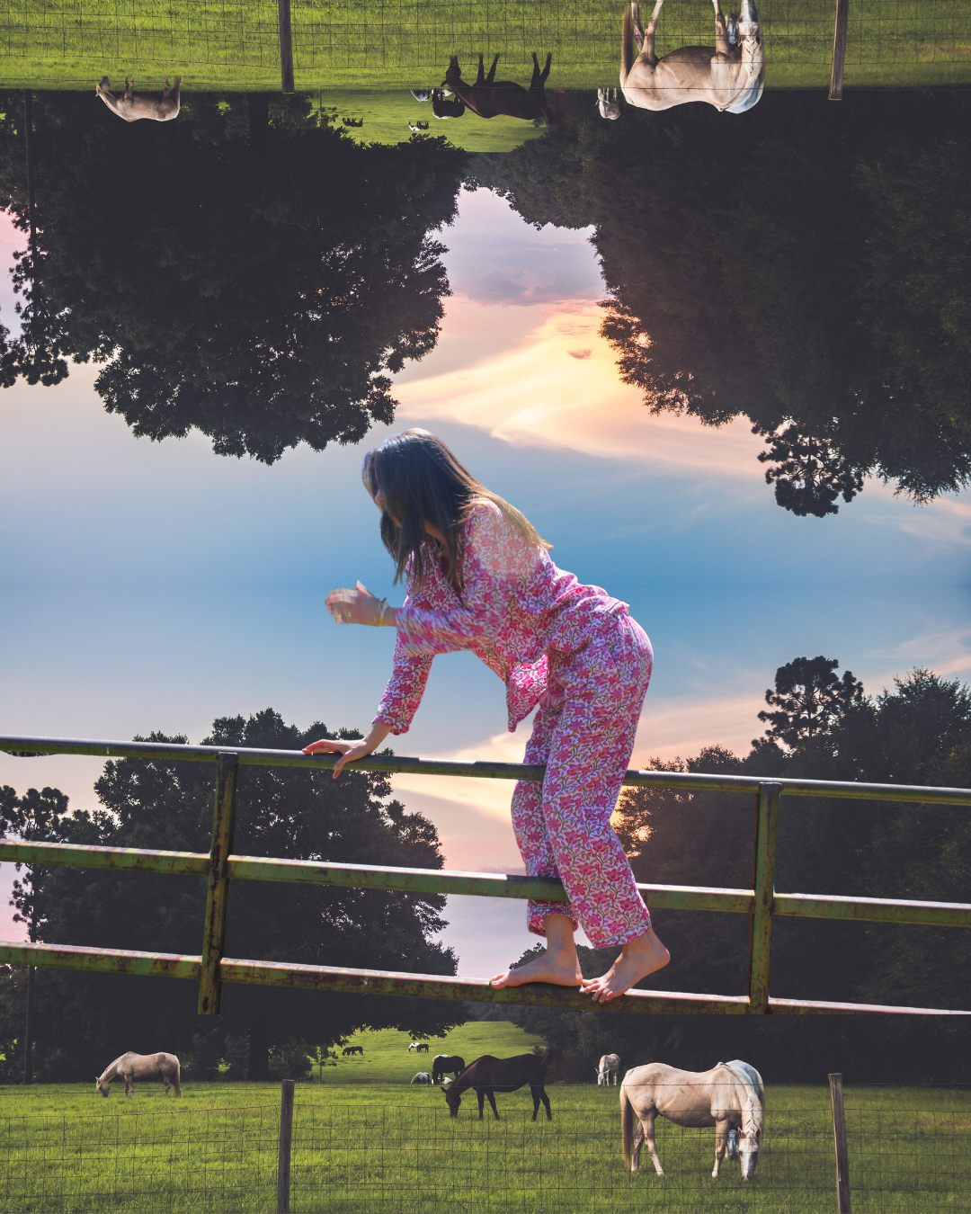 A woman in pink floral pajamas balancing on a narrow metal railing in a field with horses grazing, with trees and a sunset sky in the background. The image is upside down.