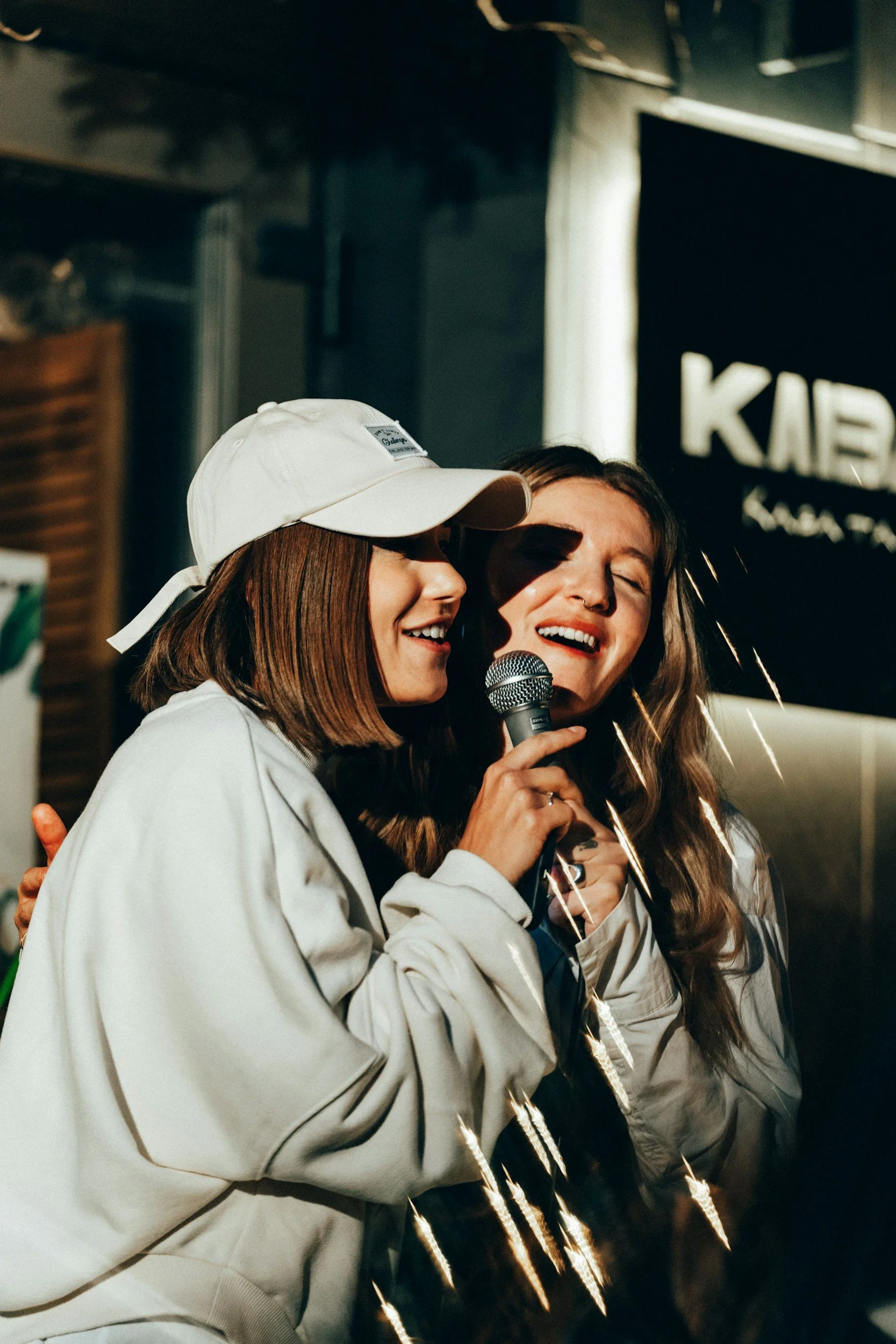 Two women singing into a microphone during a karaoke night, smiling and enjoying themselves.