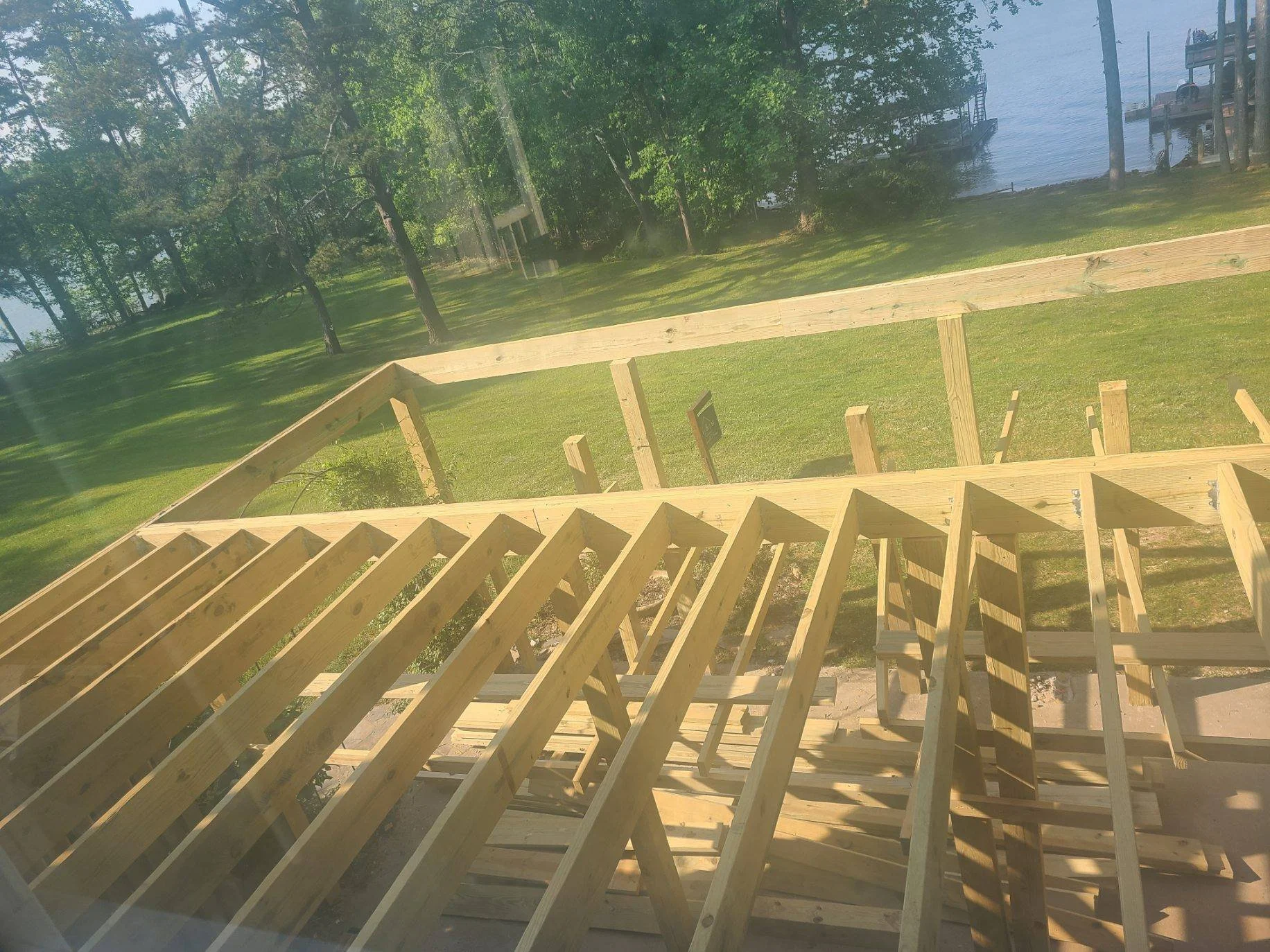 Wooden staircase under construction leading down to a grassy lawn with trees and a water body in the background.