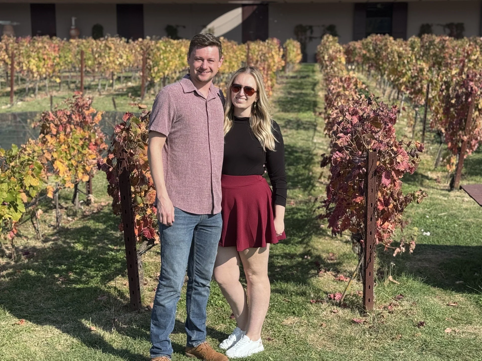 A man and woman standing together in a vineyard with grapevines turning colors in the fall.
