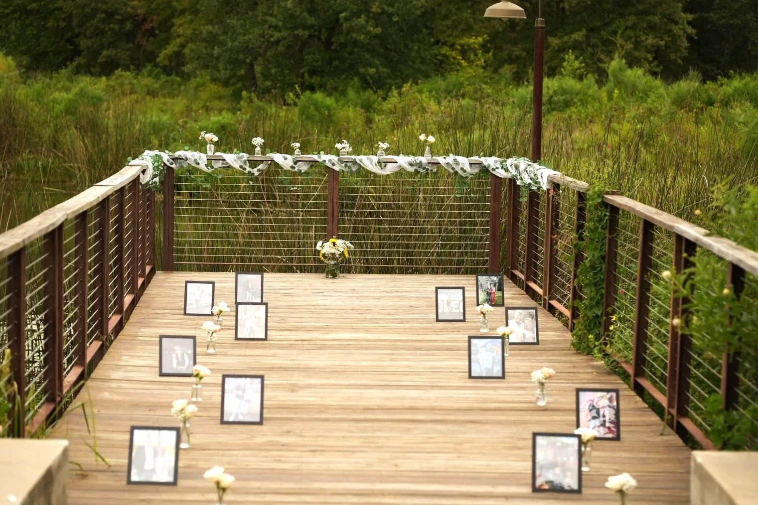 Outdoor wooden deck decorated for a wedding, with framed photos and small flower arrangements.