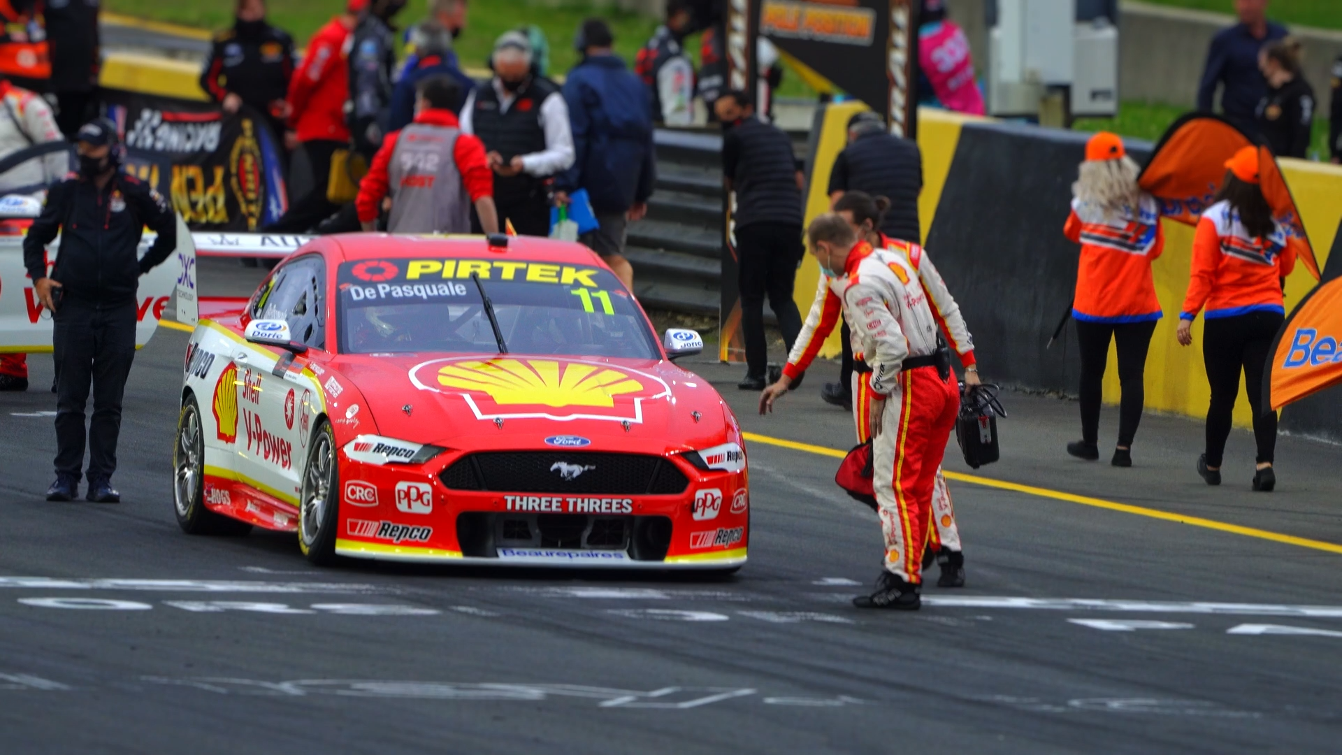 A red race car on a track with pit crew and spectators in the background, part of a racing event.
