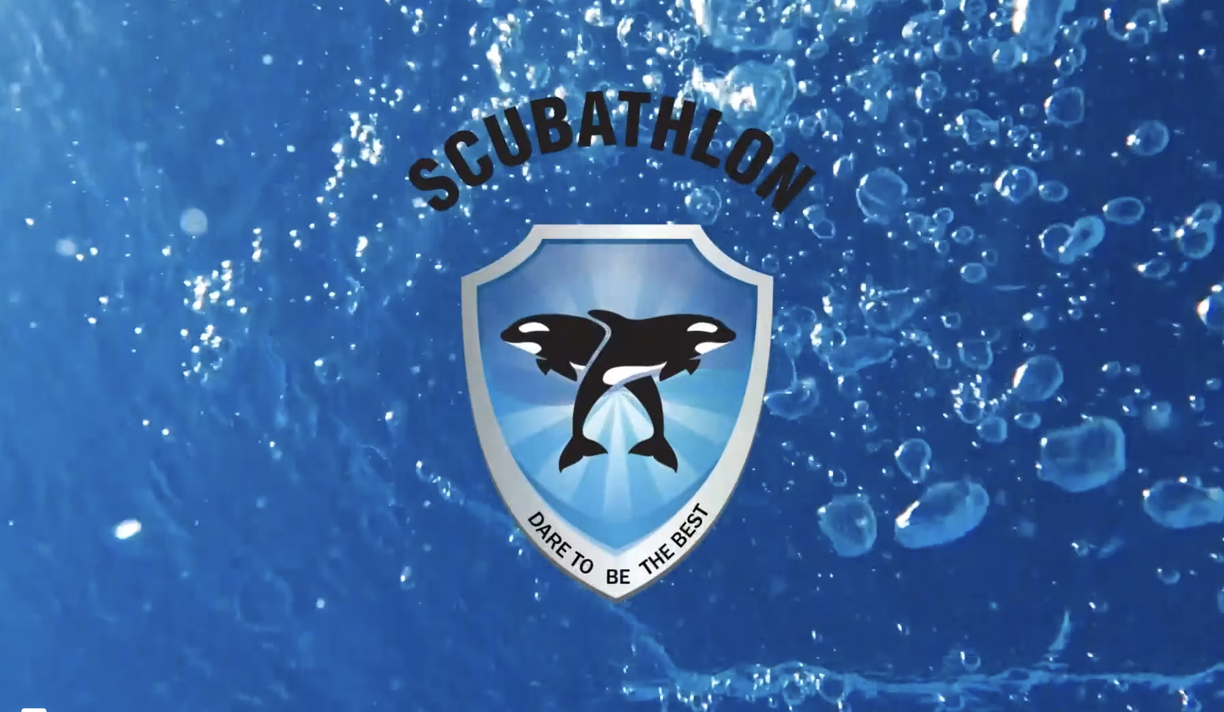 Underwater scene with bubbles and a logo for a scuba diving organization featuring a black fish inside a shield with the text 'SCUBATHLON' on top and 'DARE TO BE THE BEST' at the bottom.