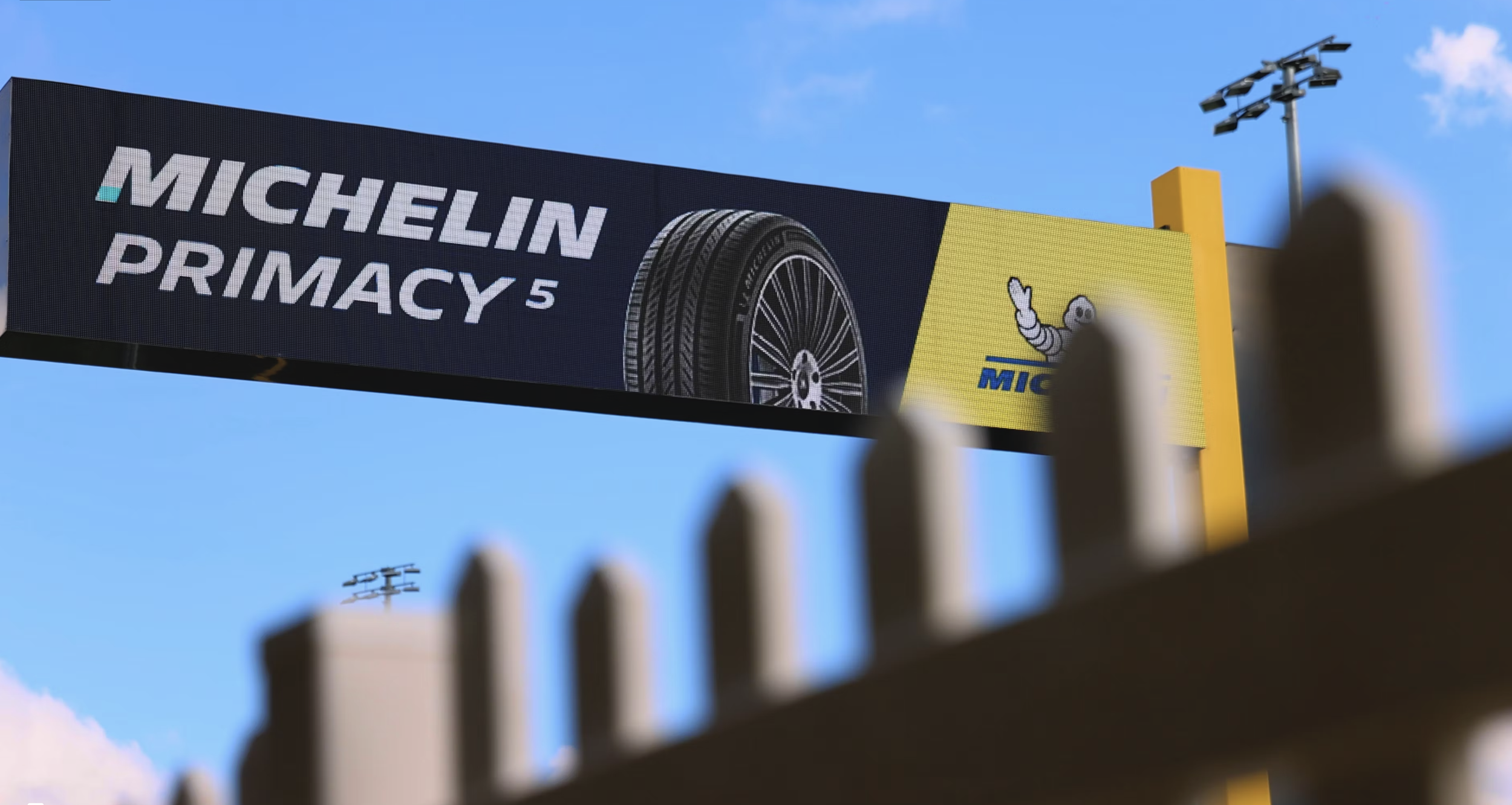 Billboard advertising Michelin Primacy 5 tires with a logo of the Michelin mascot, the Michelin man, visible on a bright yellow background, under a clear blue sky.