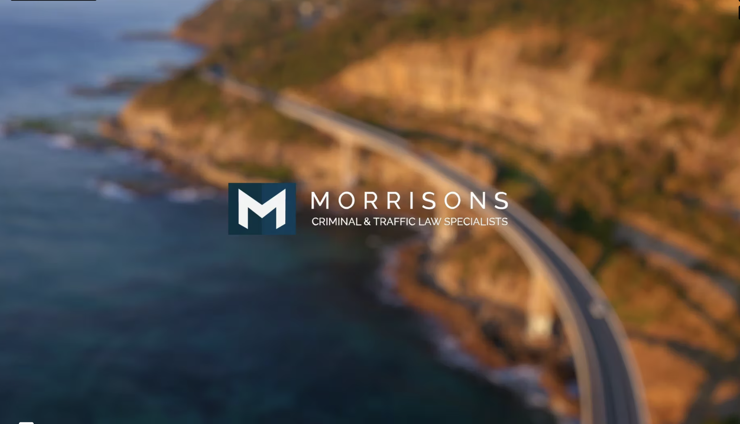 Blurry aerial view of a coastal highway curving along cliffs with water on one side and land on the other, overlaid with the brown logo and text for Morrisons Criminal & Traffic Law Specialists.